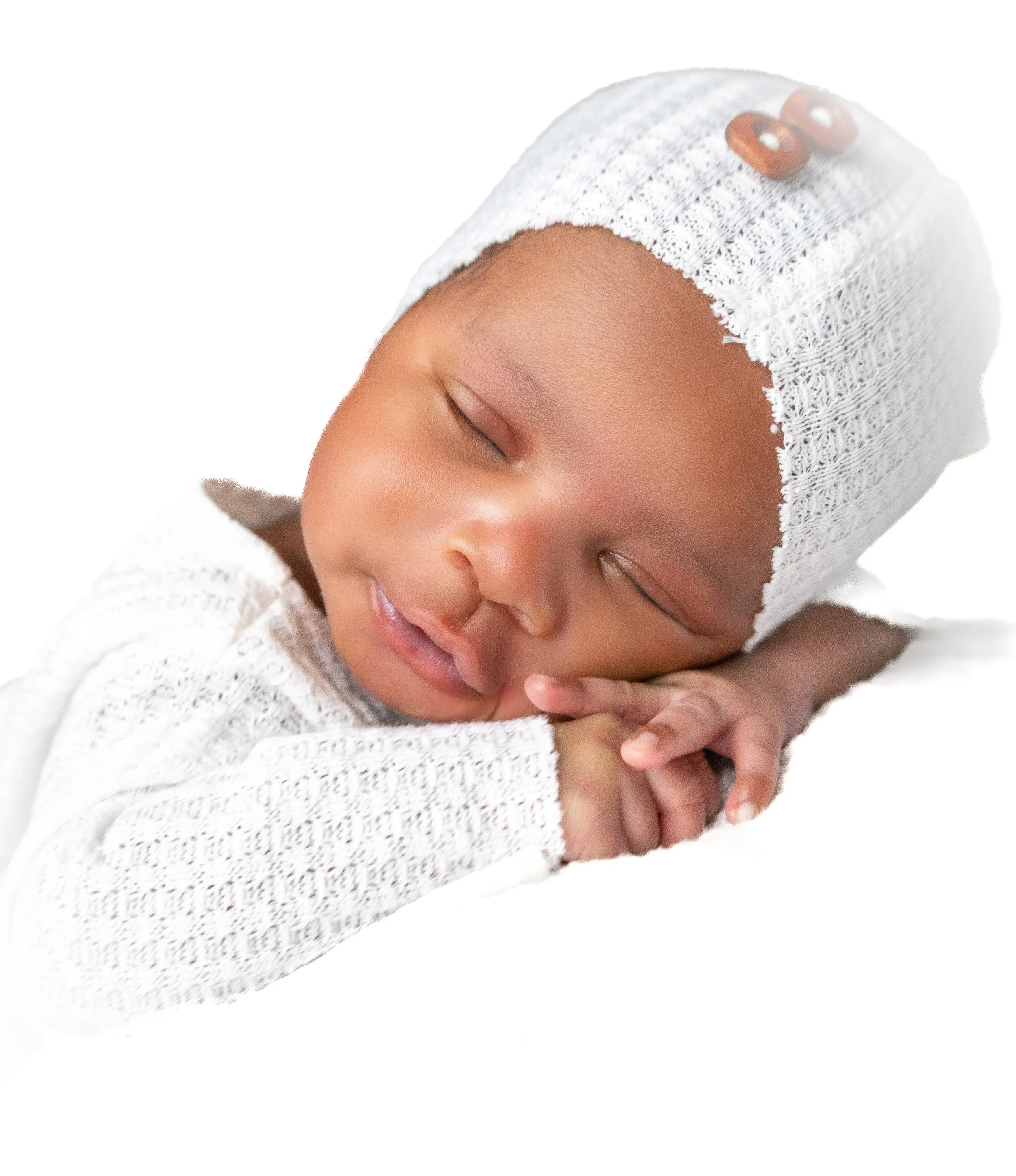 Close-up of a sleeping baby with a knit hat and a sweater, resting on a white surface.