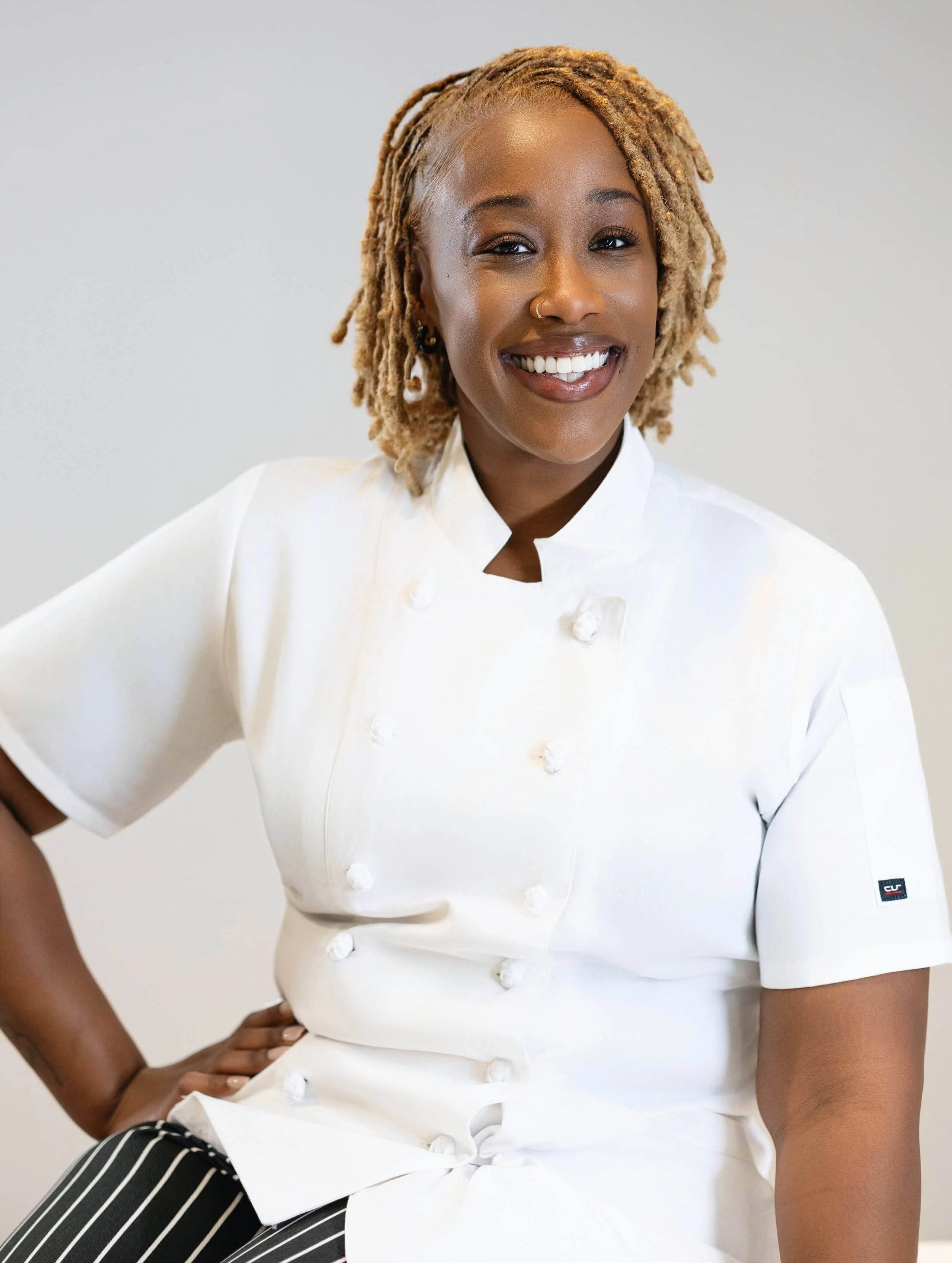 Portrait of a woman in a white chef's coat, smiling and standing with one hand on her hip. branding photography