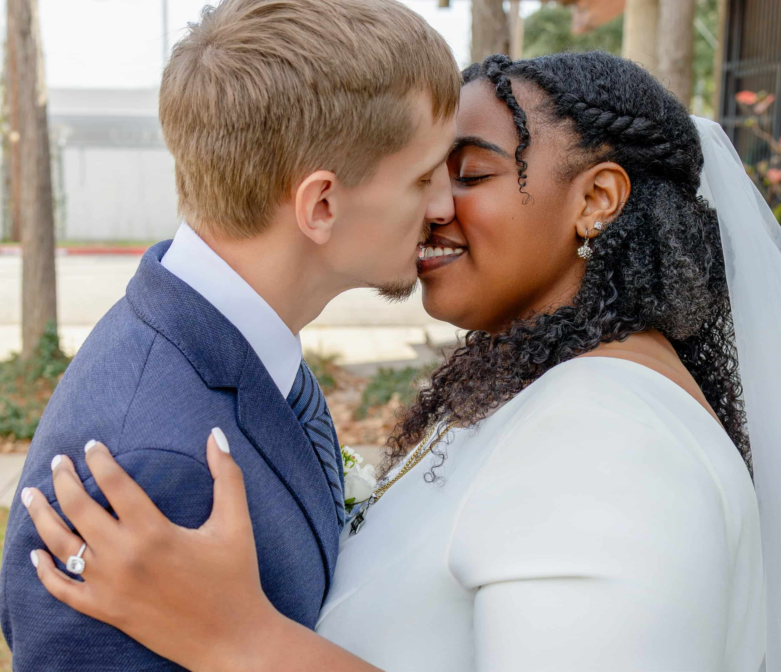 A newlywed couple sharing an intimate moment outdoors, about to kiss, with greenery and trees in the background. wedding photography