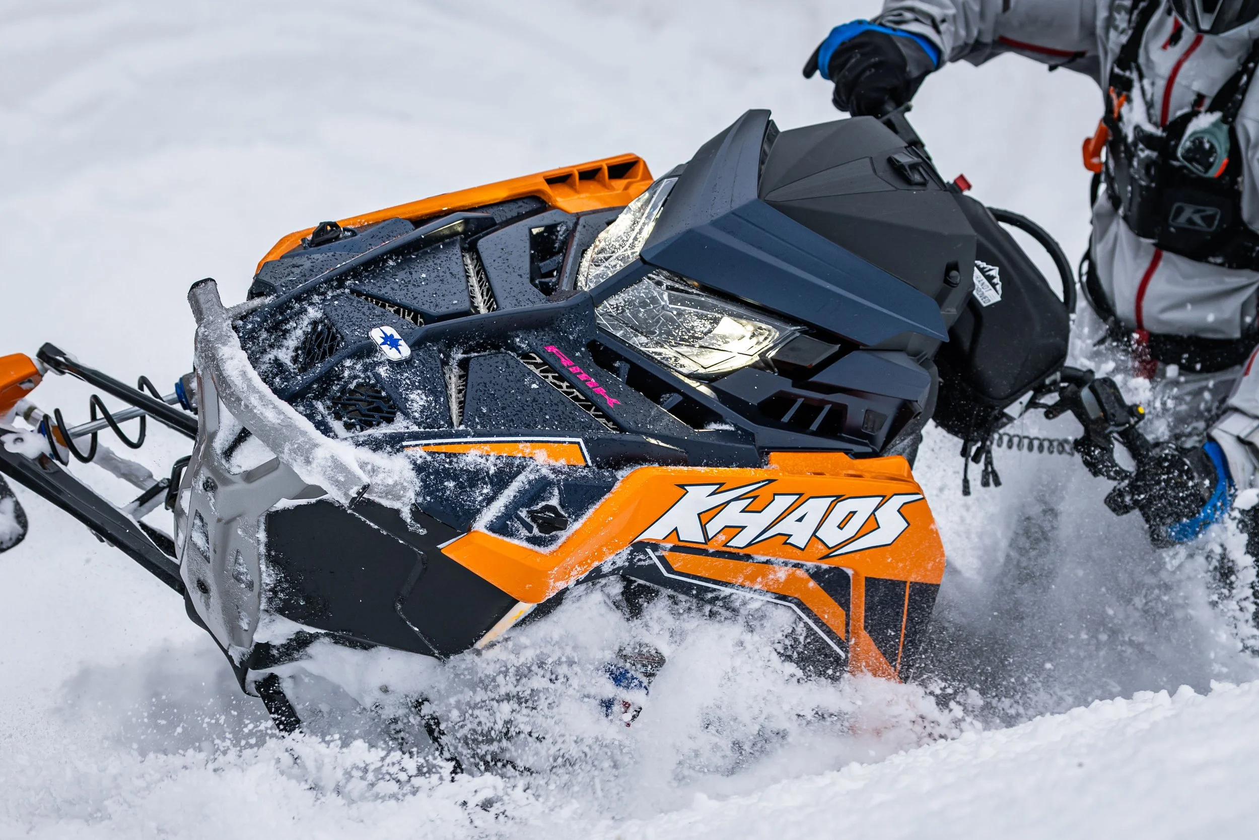 A person riding an orange and black snowmobile through snow.