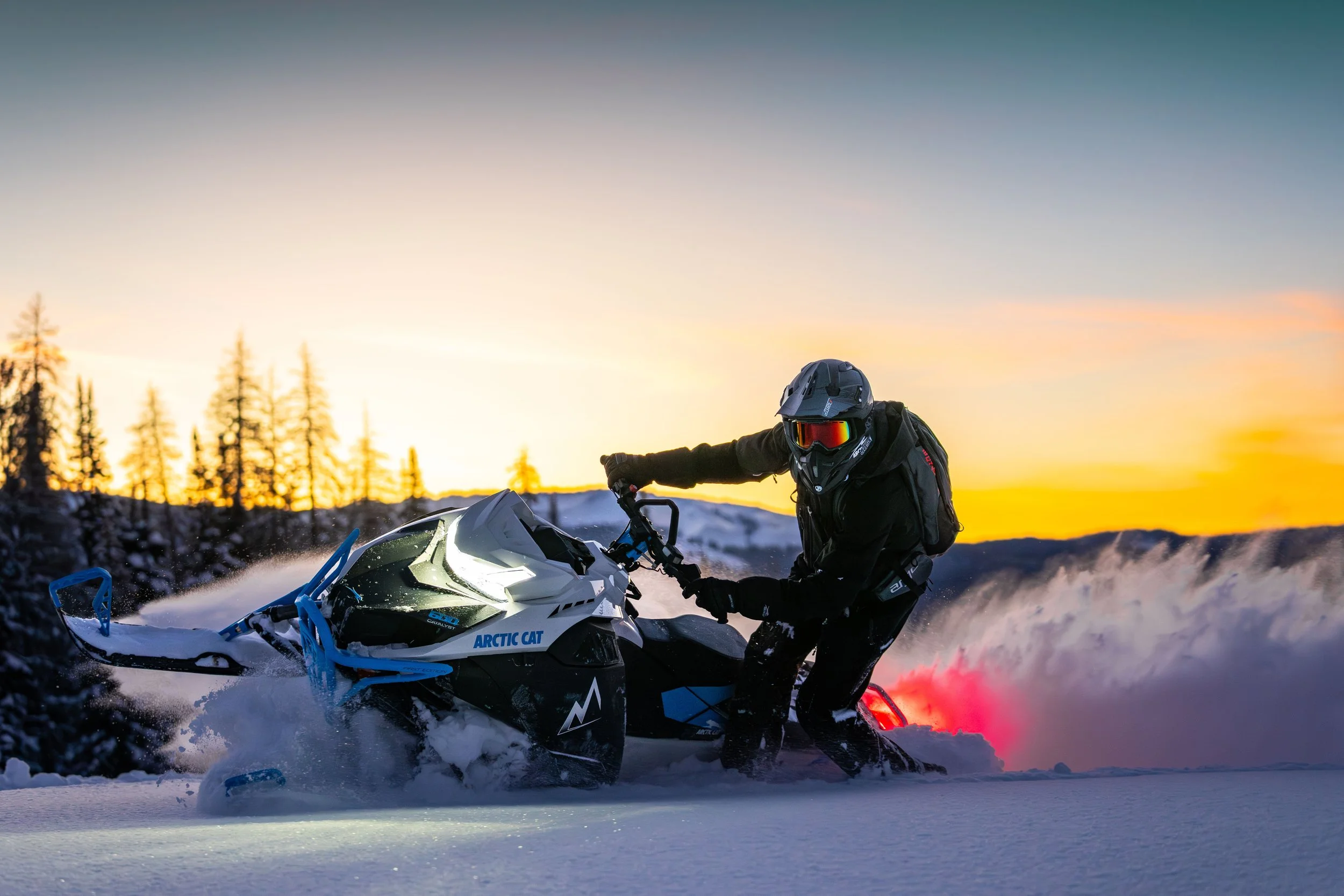 Person riding a snowmobile in snowy landscape during sunset or sunrise.