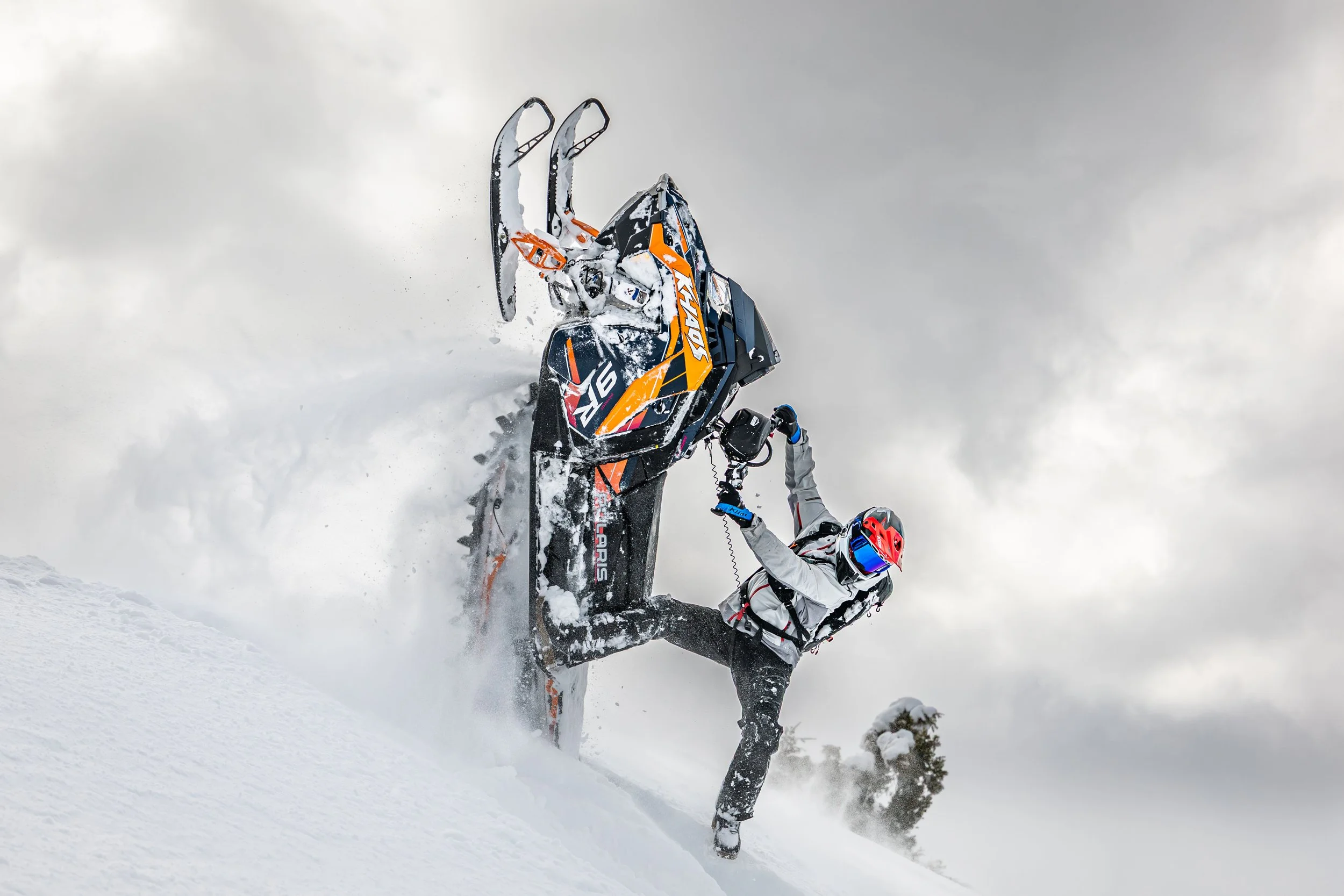 A person riding a snowmobile on a snowy slope during cloudy weather.