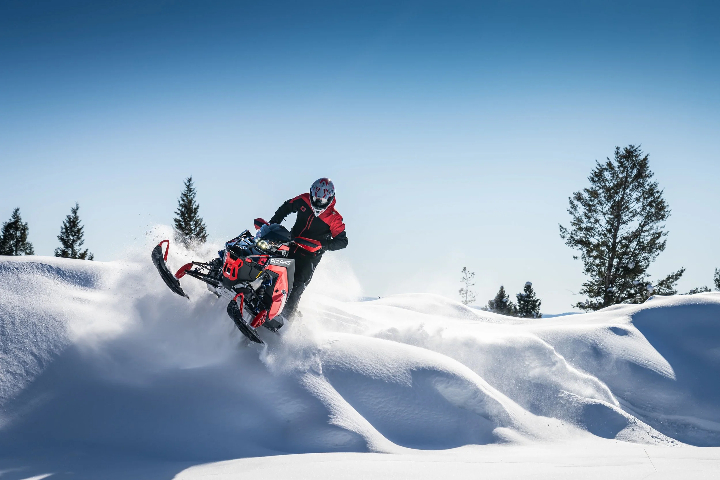 Person riding a red and black snowmobile through snow in a winter landscape.