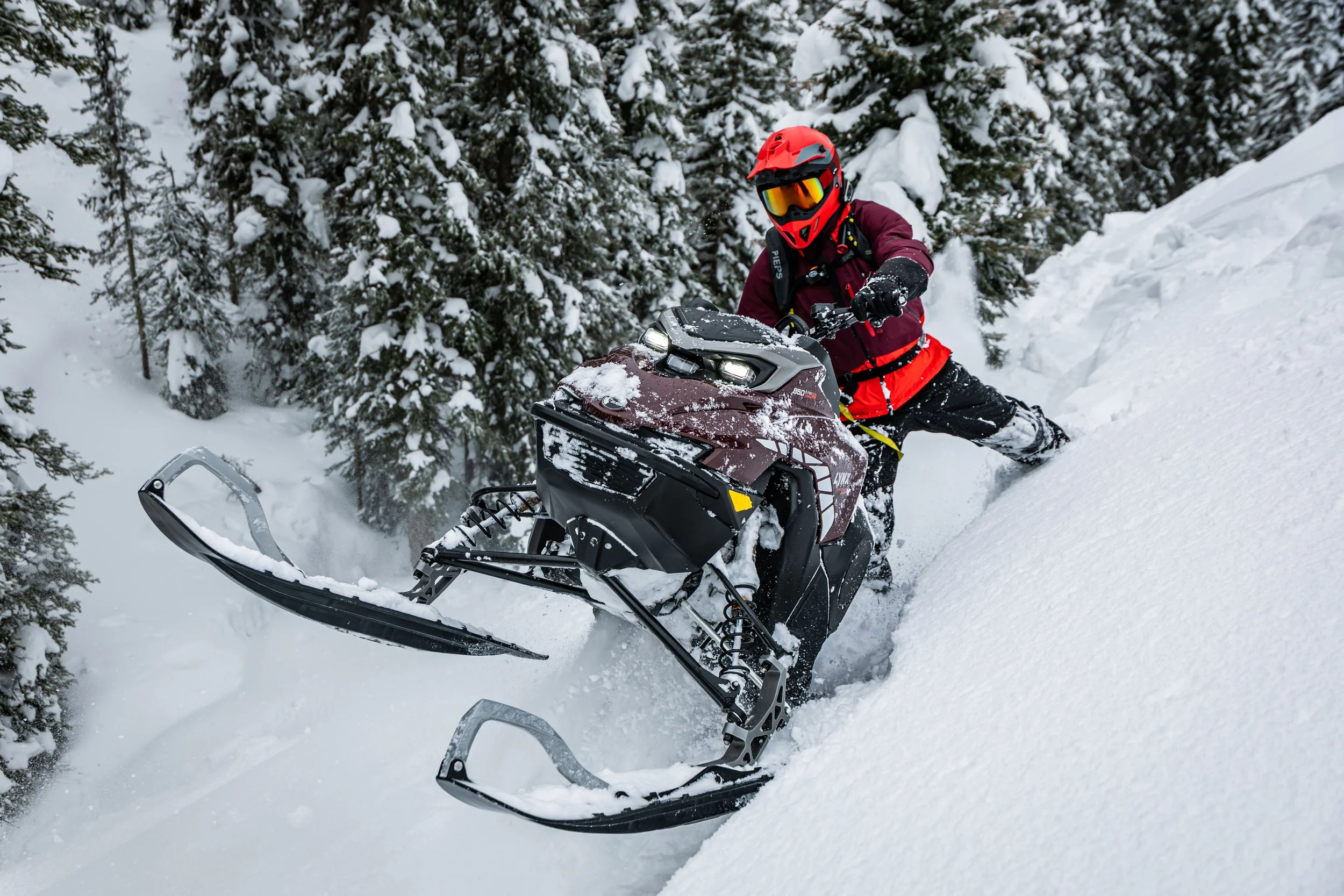 A person riding a snowmobile on a snowy slope surrounded by snow-covered trees.