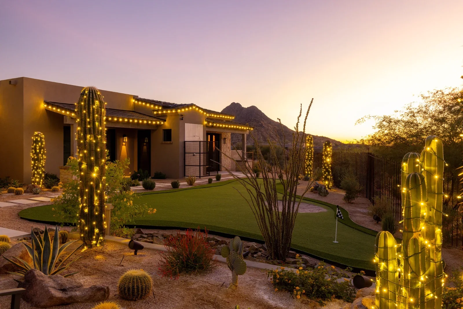 Sunset view of a desert backyard with illuminated cacti and a miniature golf course.