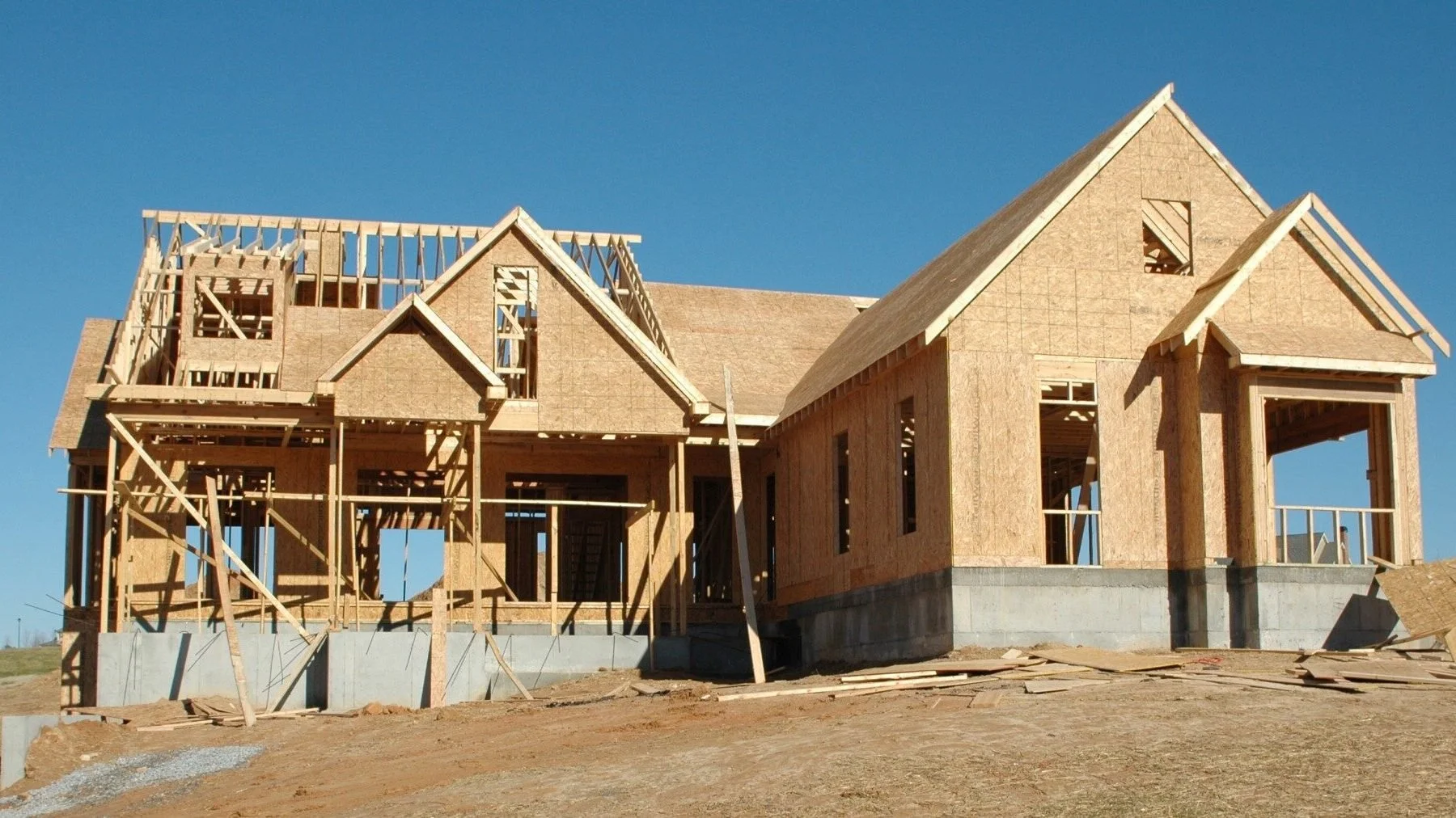 Under construction house with wooden framing and plywood walls, blue sky background.