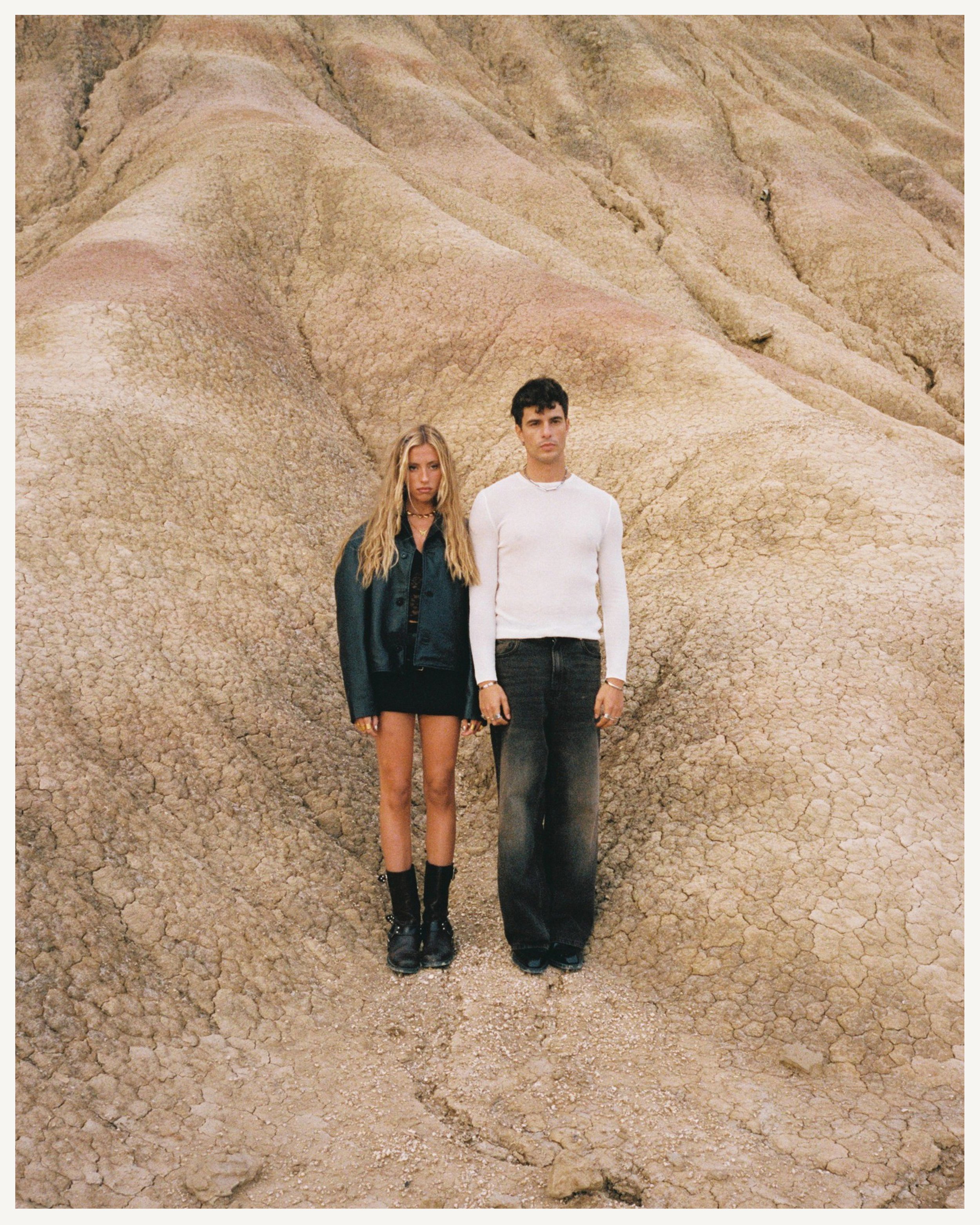 Jóvenes parados en un paisaje de tierra árida y rocas, con fondo de formaciones geológicas.