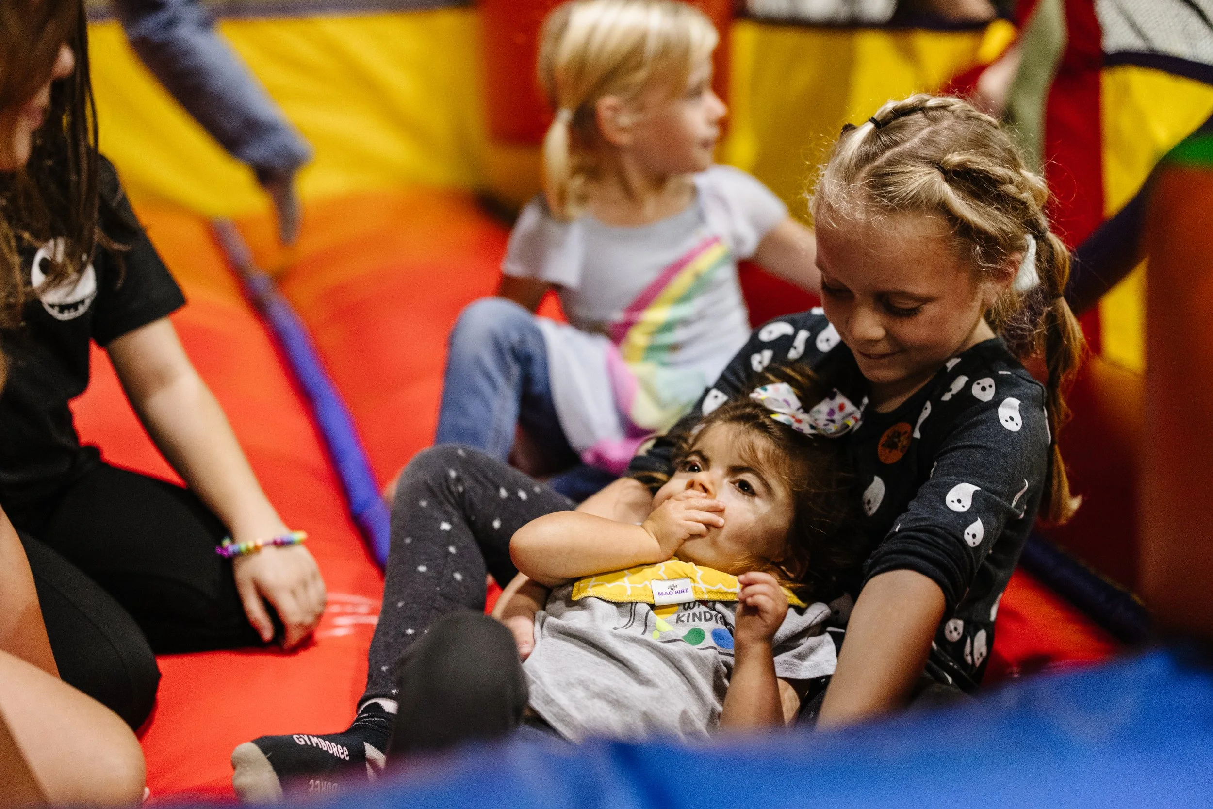 Children playing on a bounce house, with one girl comforting or playing with a younger girl who is lying down.