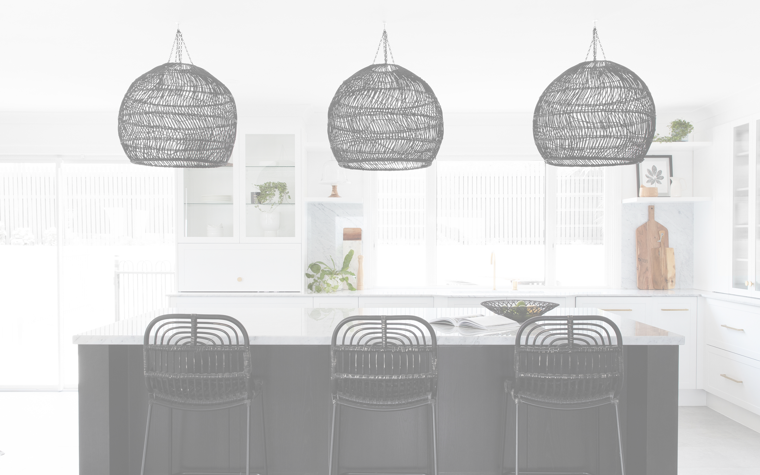 Bright, modern kitchen with white cabinetry and countertops, black wicker pendant lights over a kitchen island with three black wicker chairs.