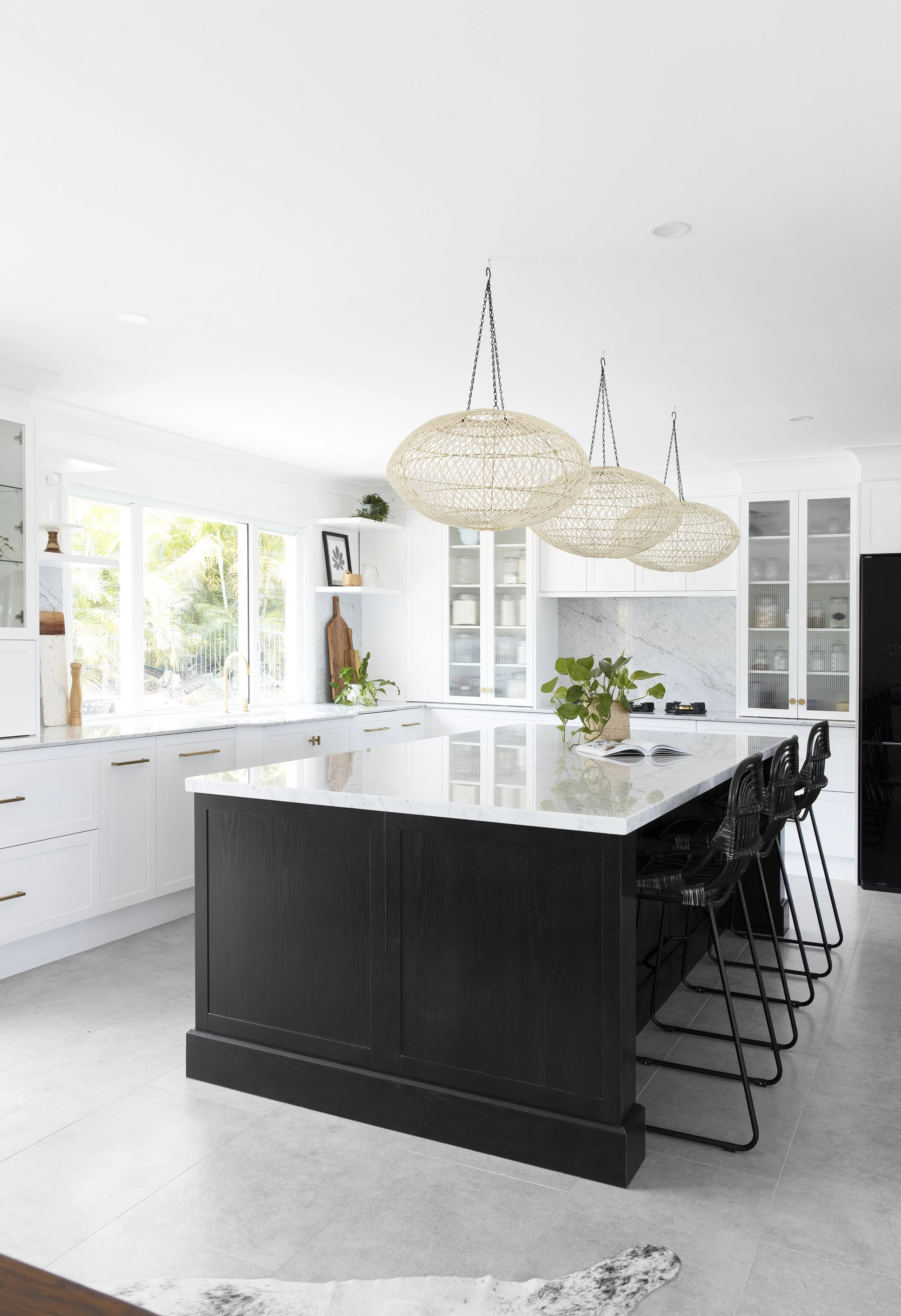 Modern white kitchen with large island, black base, white marble countertops, natural woven pendant lights, and black bar stools.