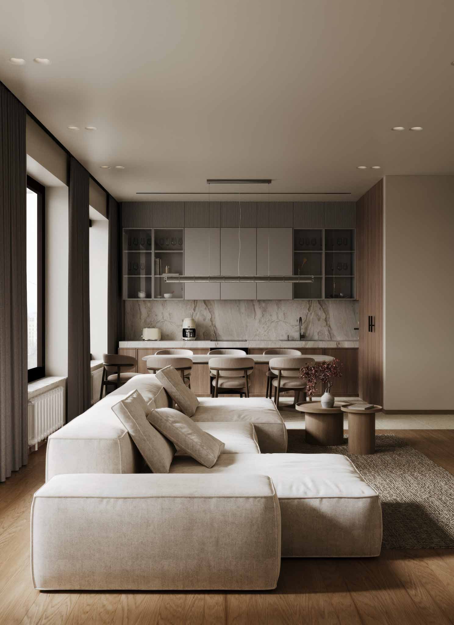 Modern living room with beige sofa, pillows, and two round coffee tables, open kitchen with bar stools, marble backsplash, and minimal decor.