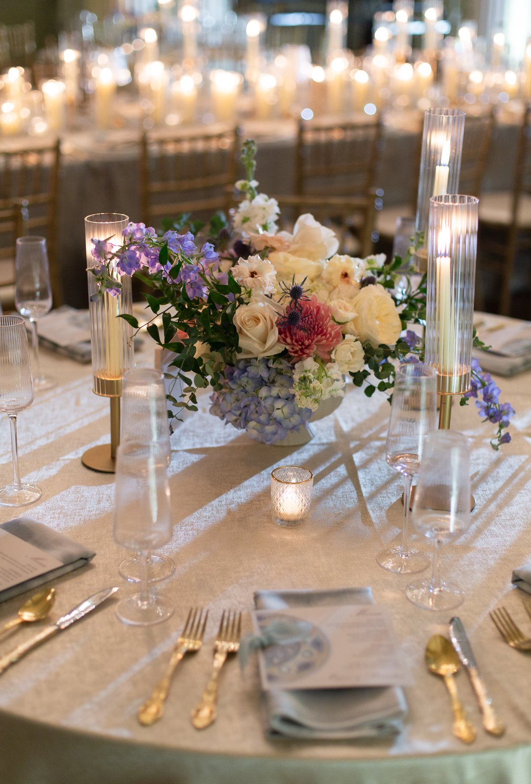 Elegant wedding reception table with floral centerpiece, candles, wine glasses, and gold utensils.
