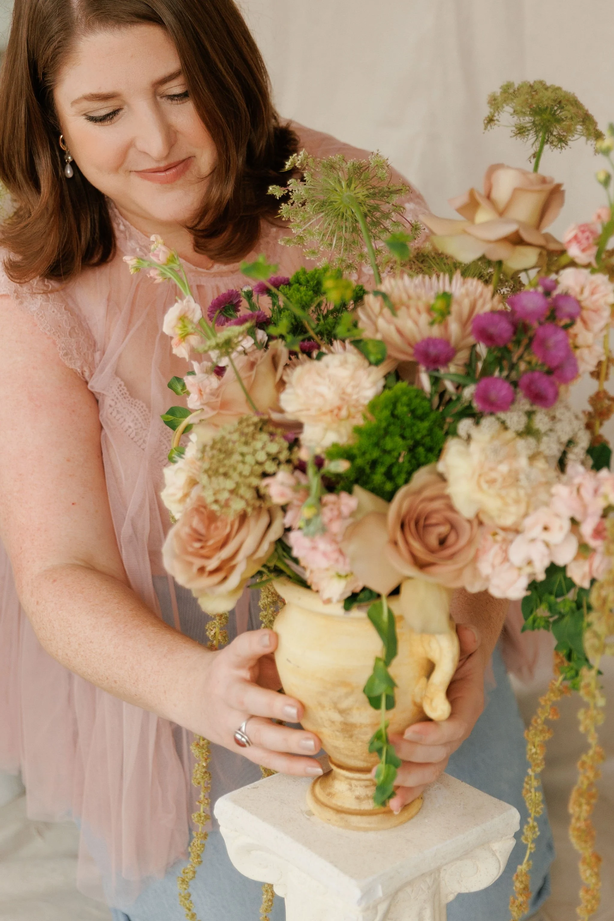A woman in a pink dress arranging a large floral bouquet in a decorative urn.