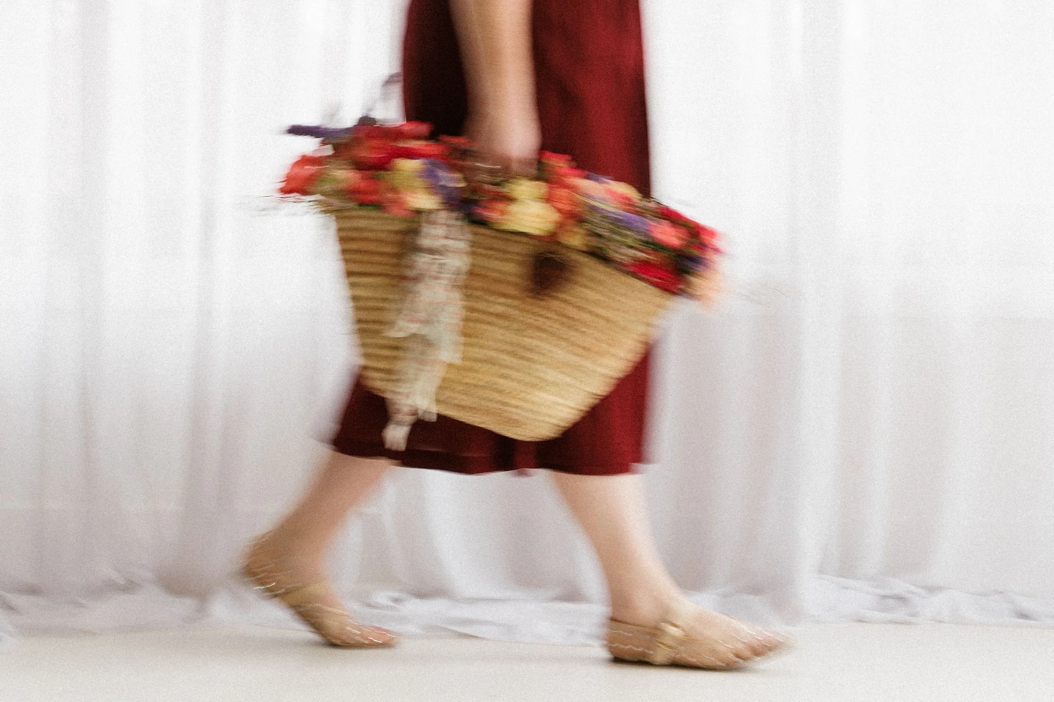 Person holding a large basket filled with colorful flowers, walking barefoot indoors.