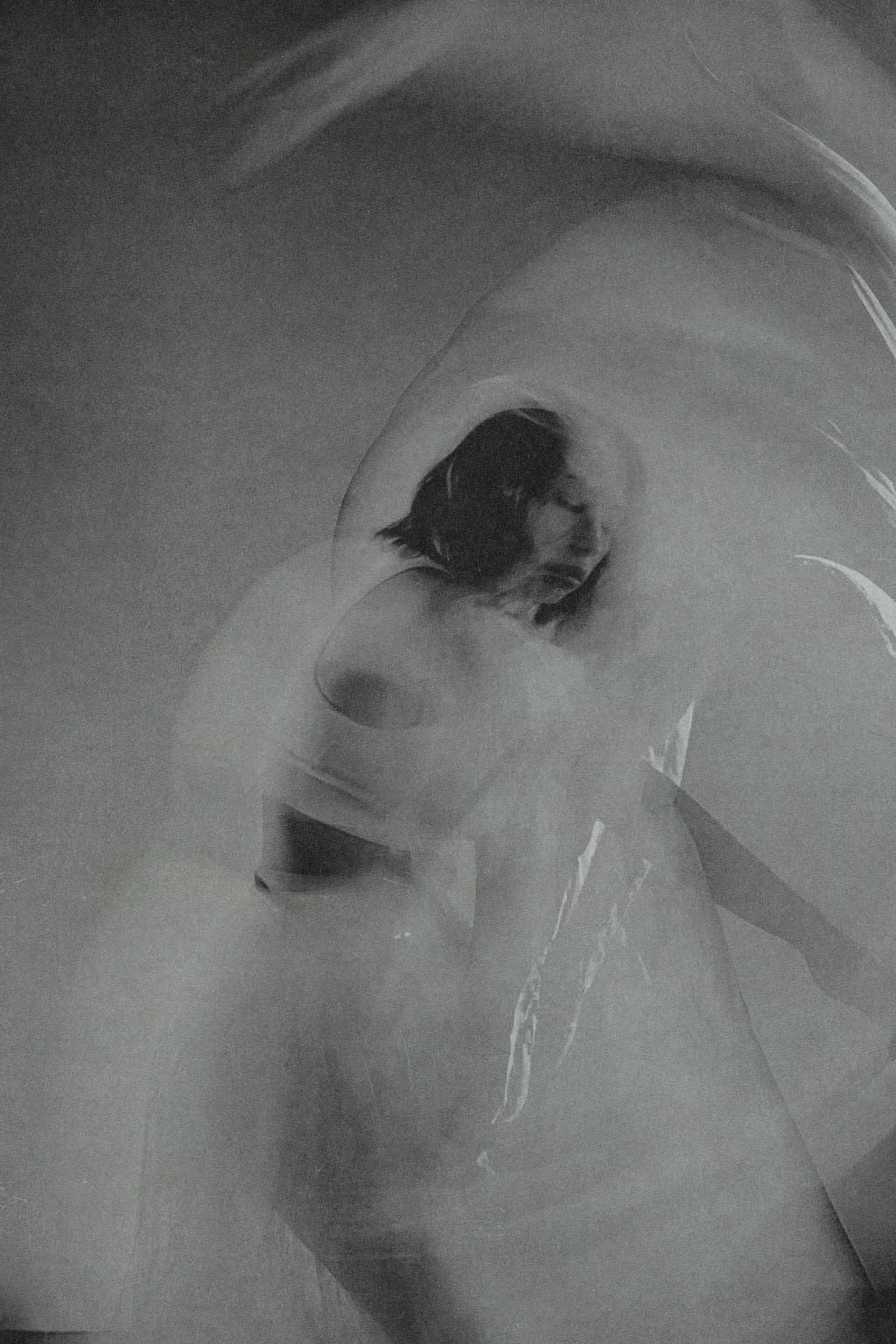 Artistic photo of a woman with dark hair, seen through a foggy or translucent surface, creating a soft, abstract effect.
