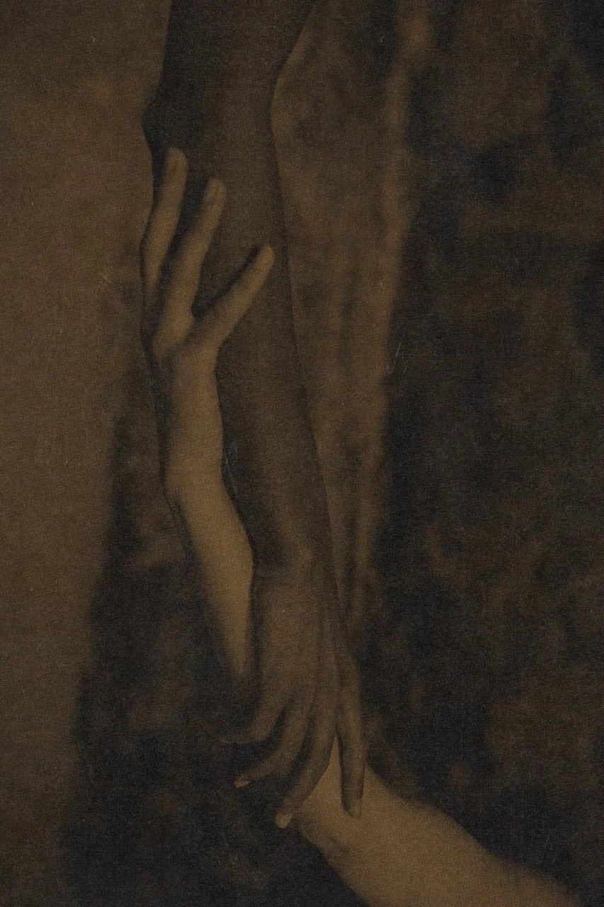 Dark, moody photo of two hands gently touching each other's arms.