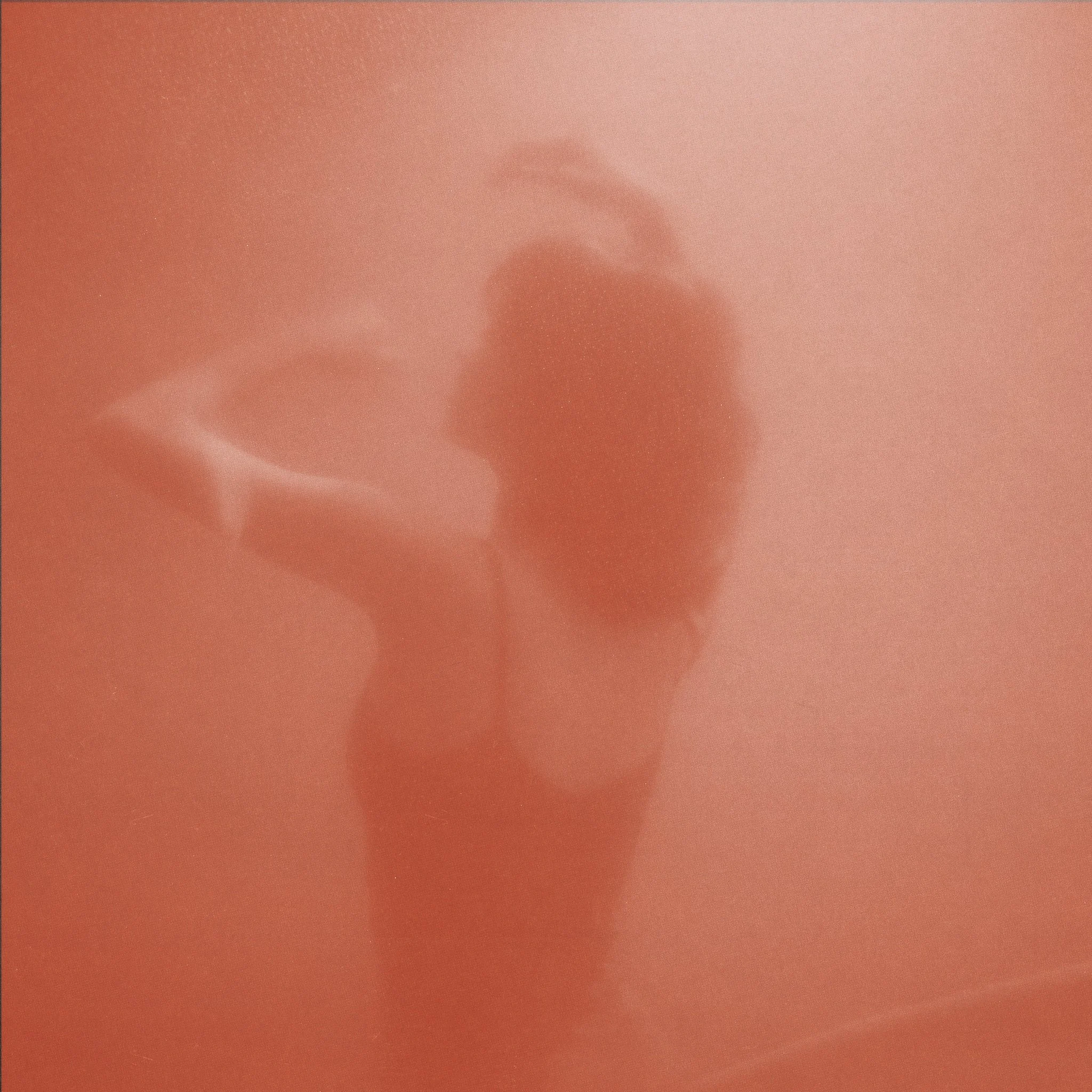 Blurred mirror selfie of a person with a ponytail holding a phone, against a reddish background.