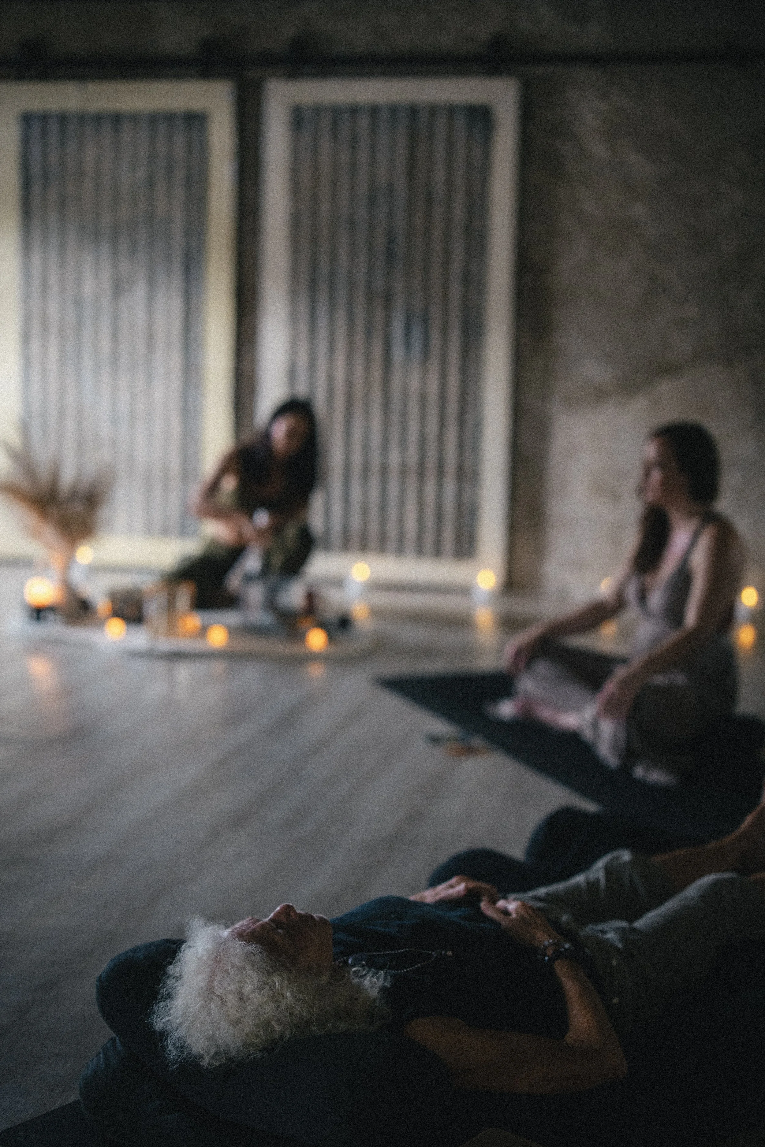 Group of women practicing yoga and meditation in a dimly lit indoor space with candles as ambiance.