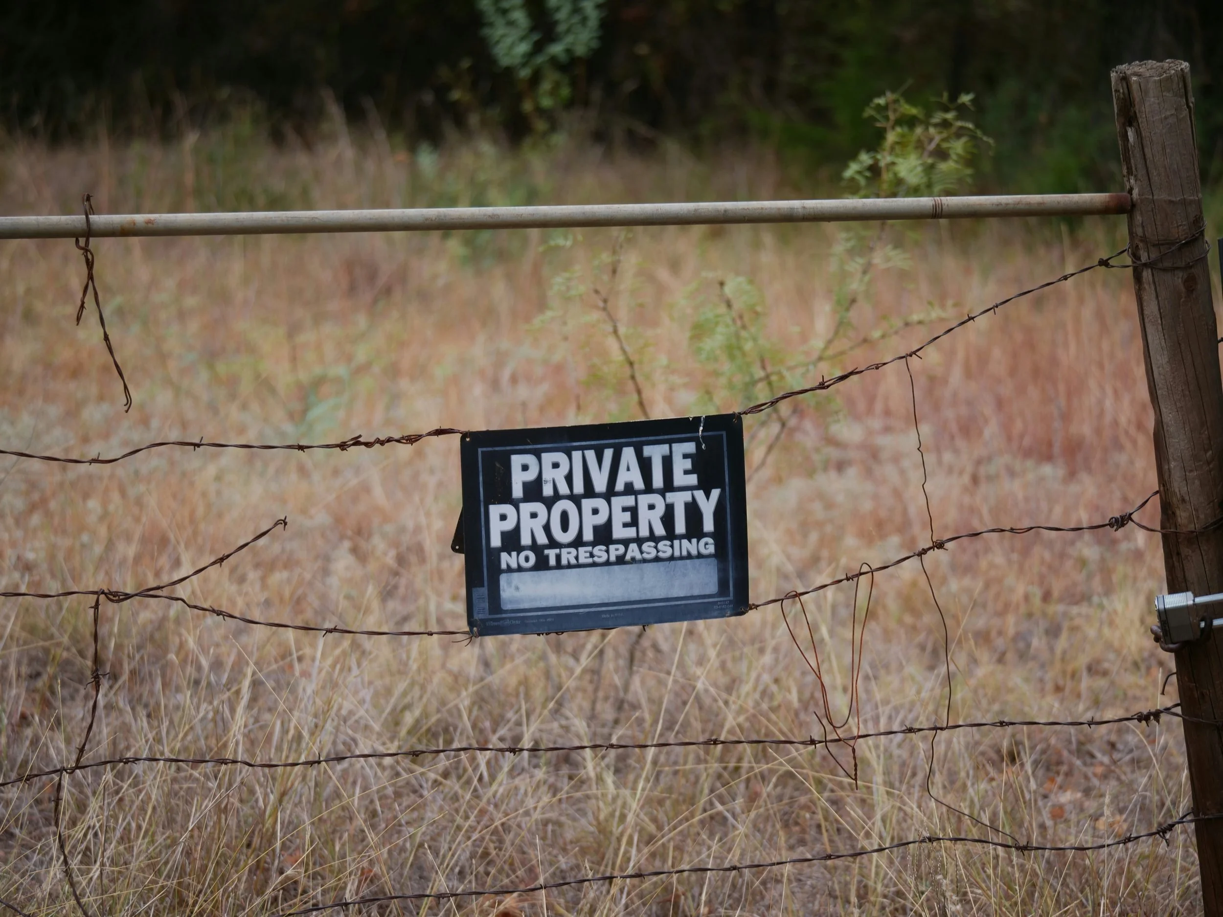 A black sign hung by wire on a rural fence with Private Property & No Trespassing on it