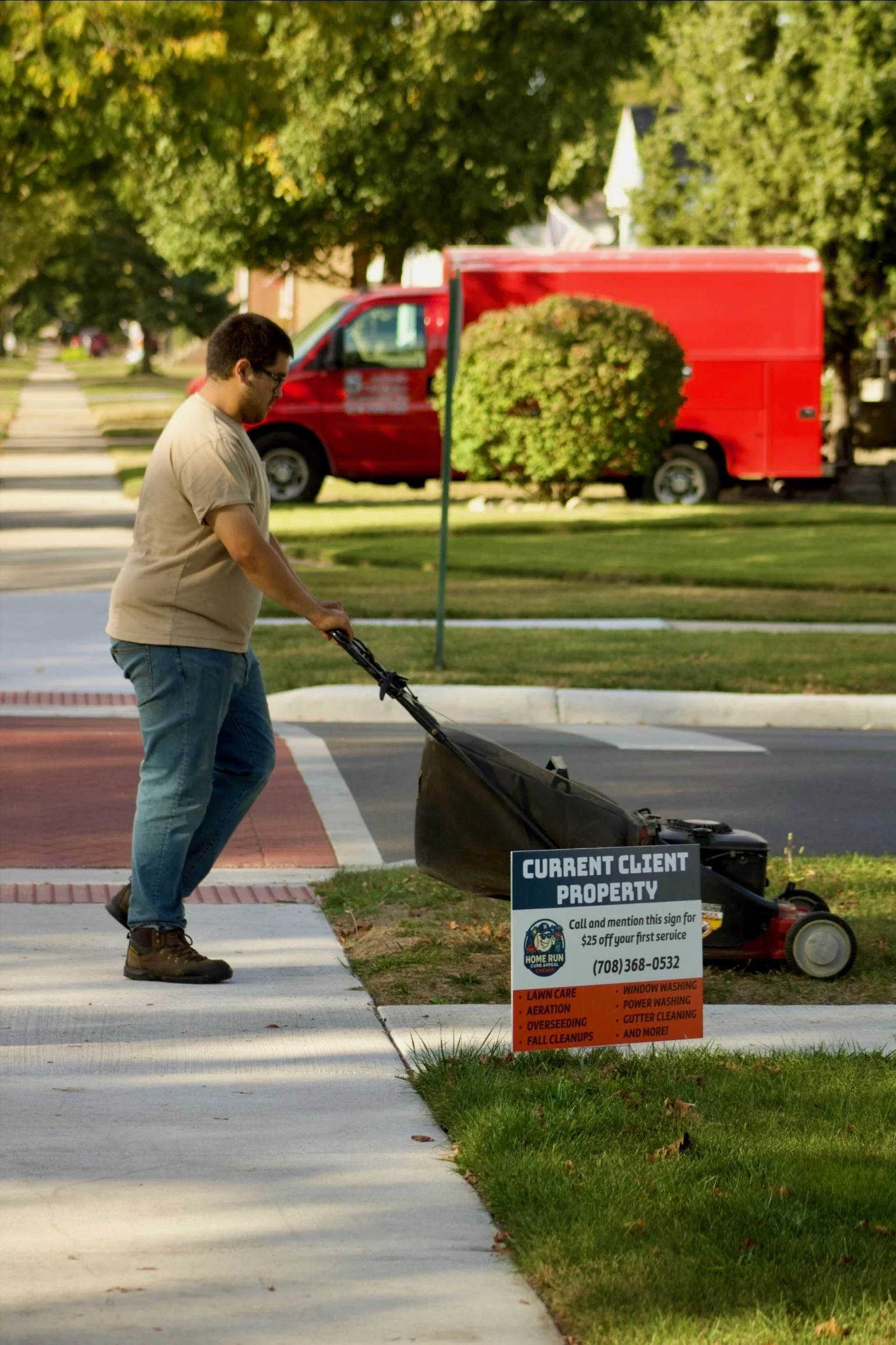 A man watering a lawn with a power washer on a sidewalk in front of a grass patch with a sign for a property maintenance service.