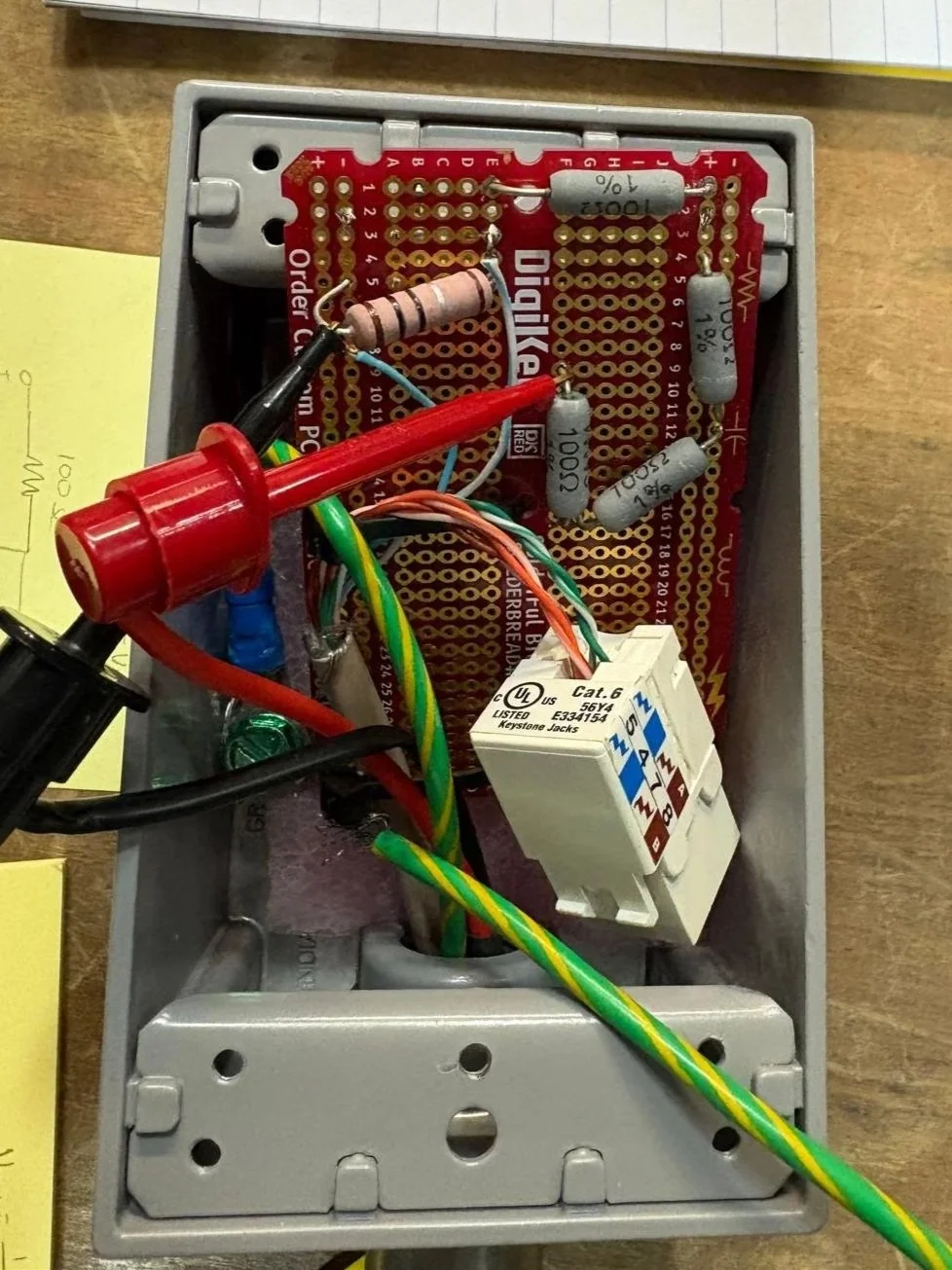 Inside of an electronic device, showing a red circuit board, resistors, wires, and a relay, all housed in a metal casing.