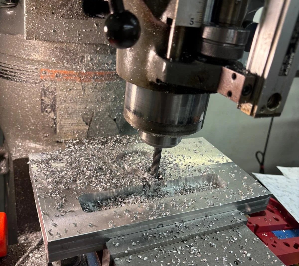 A CNC milling machine cutting metal, with metal shavings scattered on the work surface.