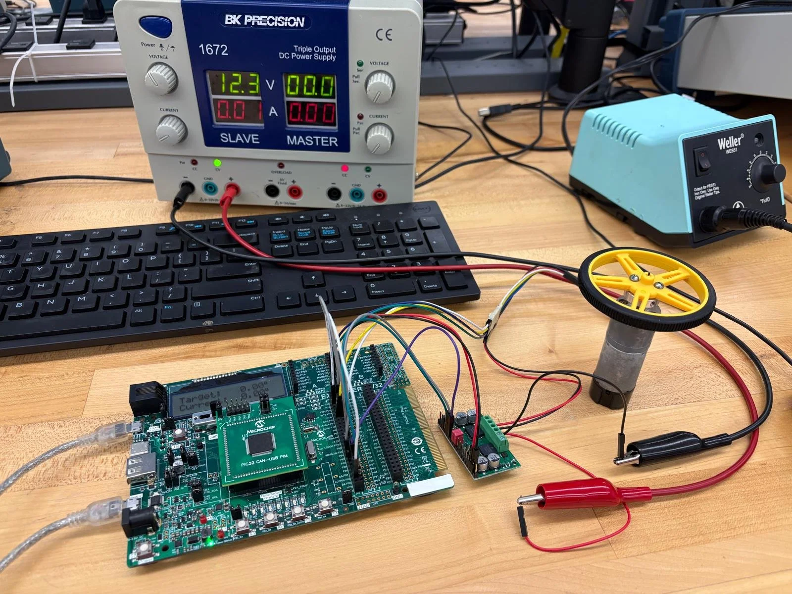 Setup of electronic testing and control circuit with a gift card microcontroller, breadboard, motor, power supplies, and a notebook keyboard on a wooden table.