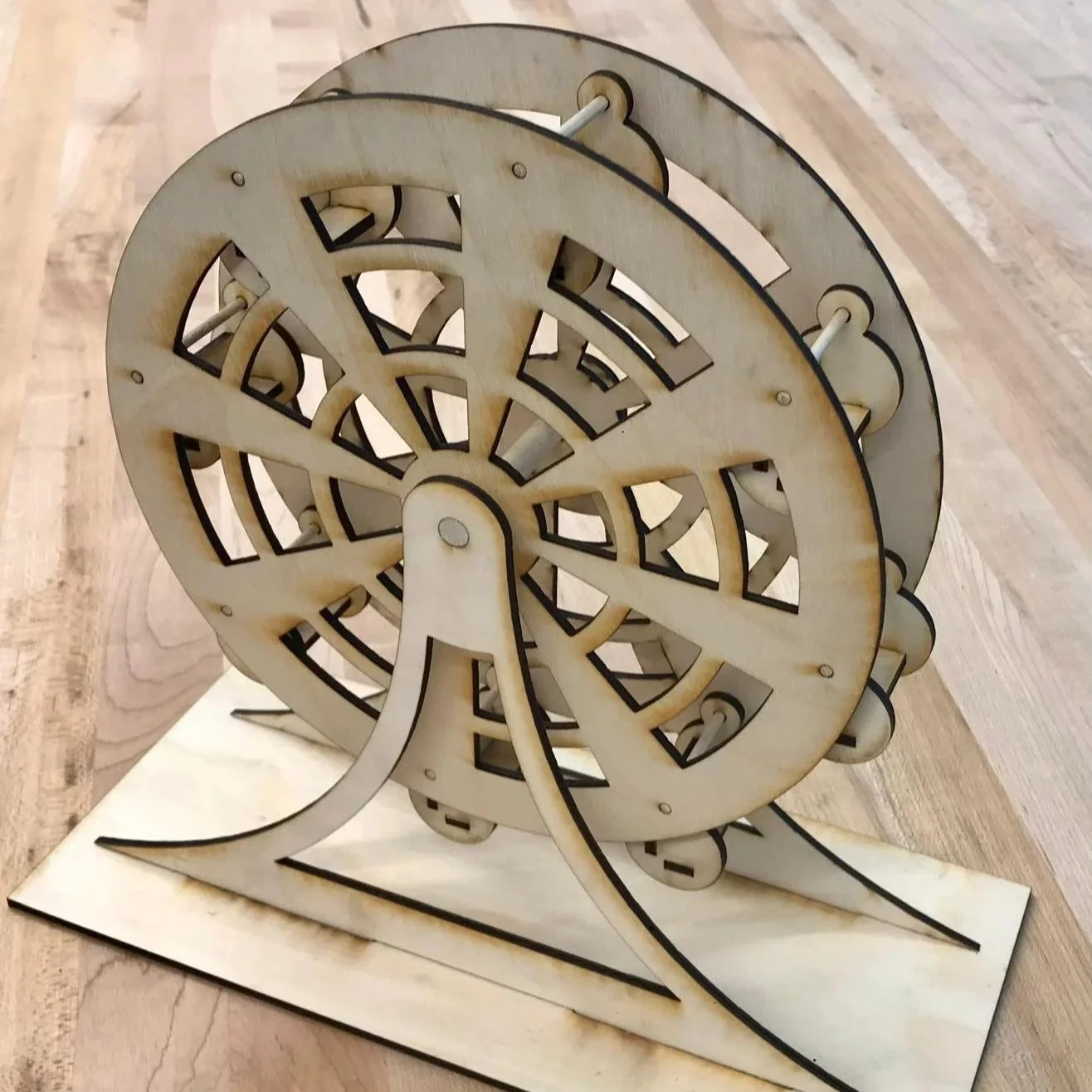 A wooden model of a Ferris wheel resting on a flat base.