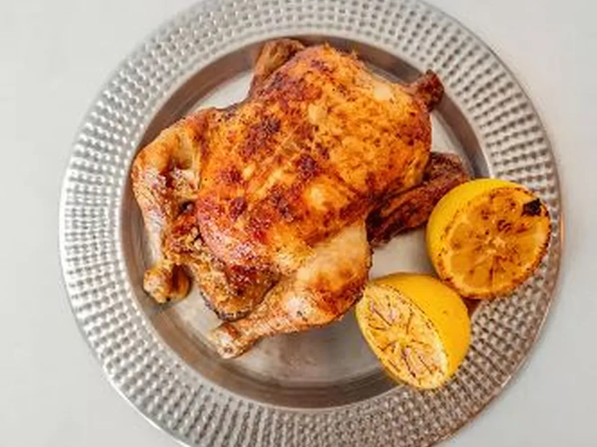 Roasted chicken with lemon halves on a silver decorative plate.