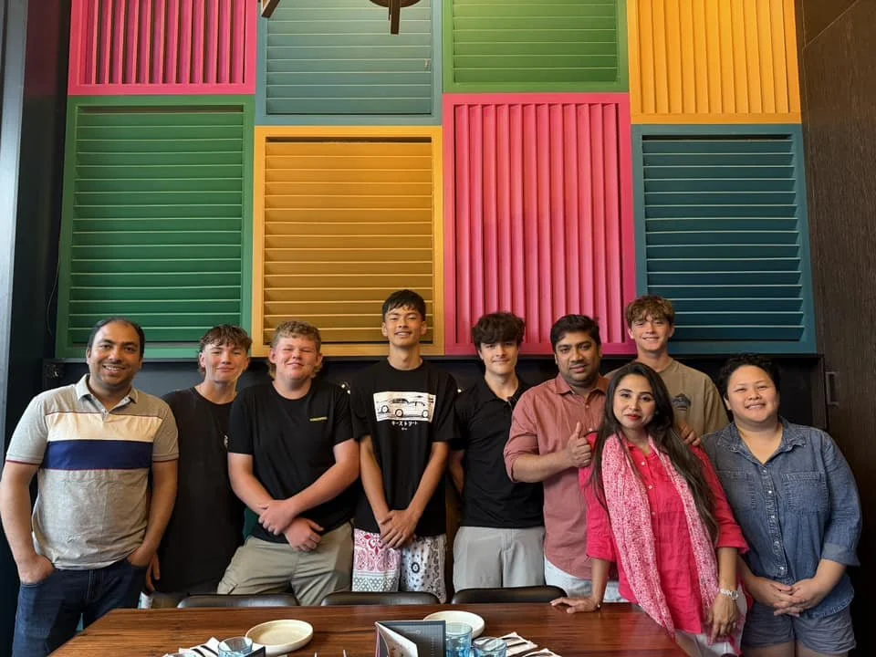 The team at Sabrina’s Grill, standing in a room with colourful wall panels in pink, green, yellow, and blue, posing for a photo behind a table with bowls and utensils.