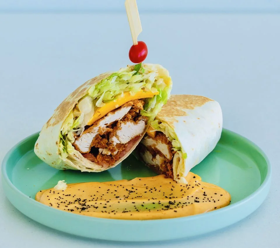 Chicken wrap cut in half, with melted cheese, lettuce, and a cherry tomato on top.