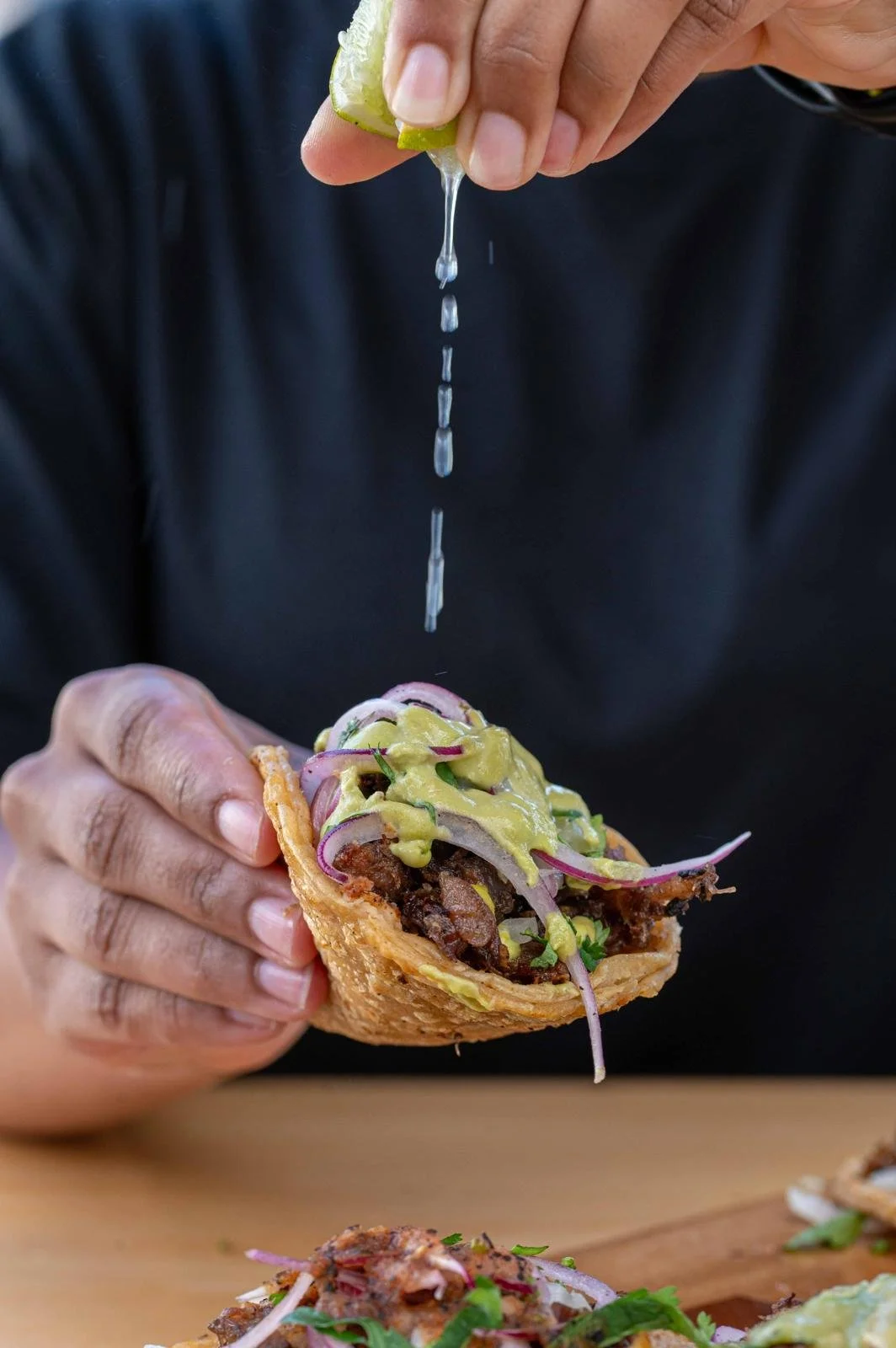 Una persona exprimiendo limón sobre un taco con carne, cebolla, cilantro y aguacate.