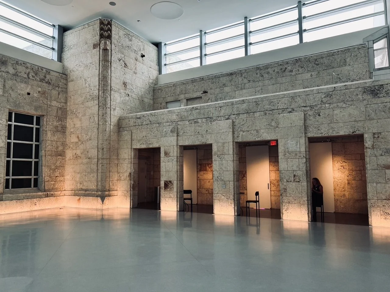 Interior of a building with stone walls, multiple doorways, and a woman in black inside one of the rooms.