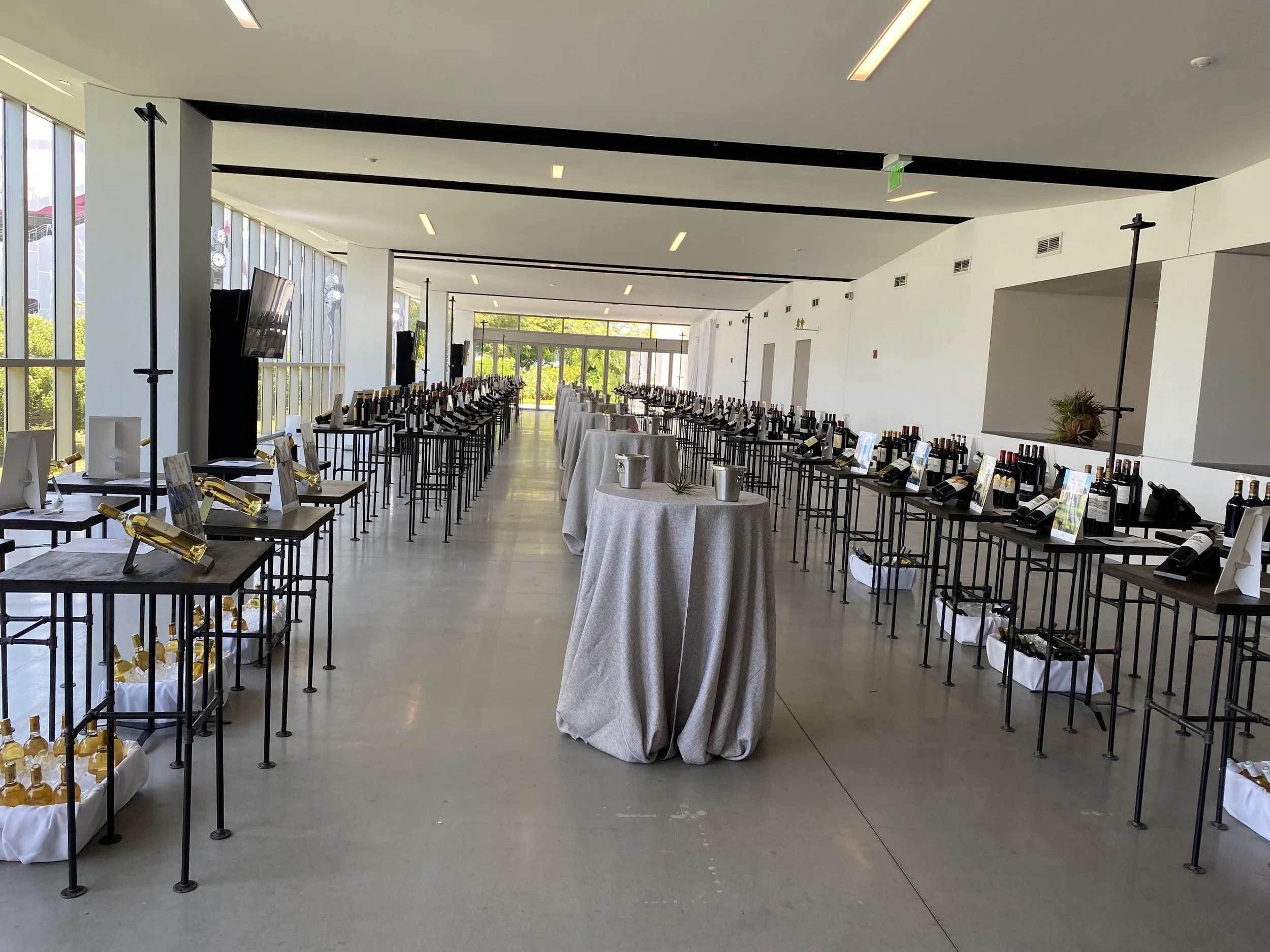 Interior of a modern venue with long tables displaying bottles of wine, wine glasses, and small display cards, set up for a tasting event or wine exhibition.