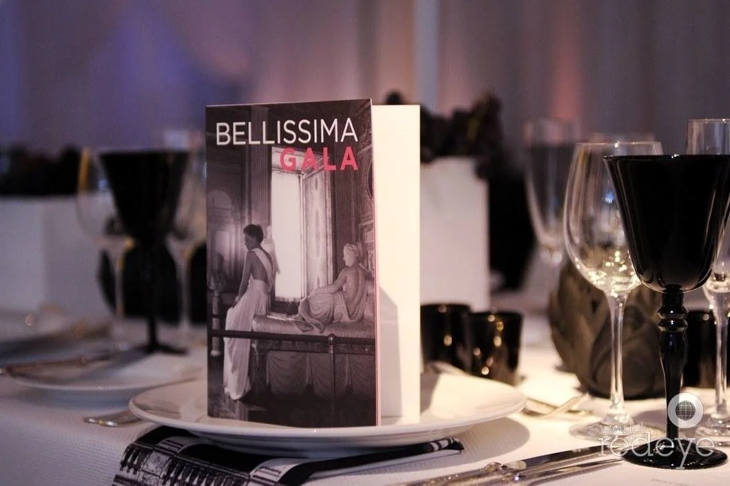 A table setting at the Bellissima Gala event with a menu card, wine glasses, and black and white tableware.
