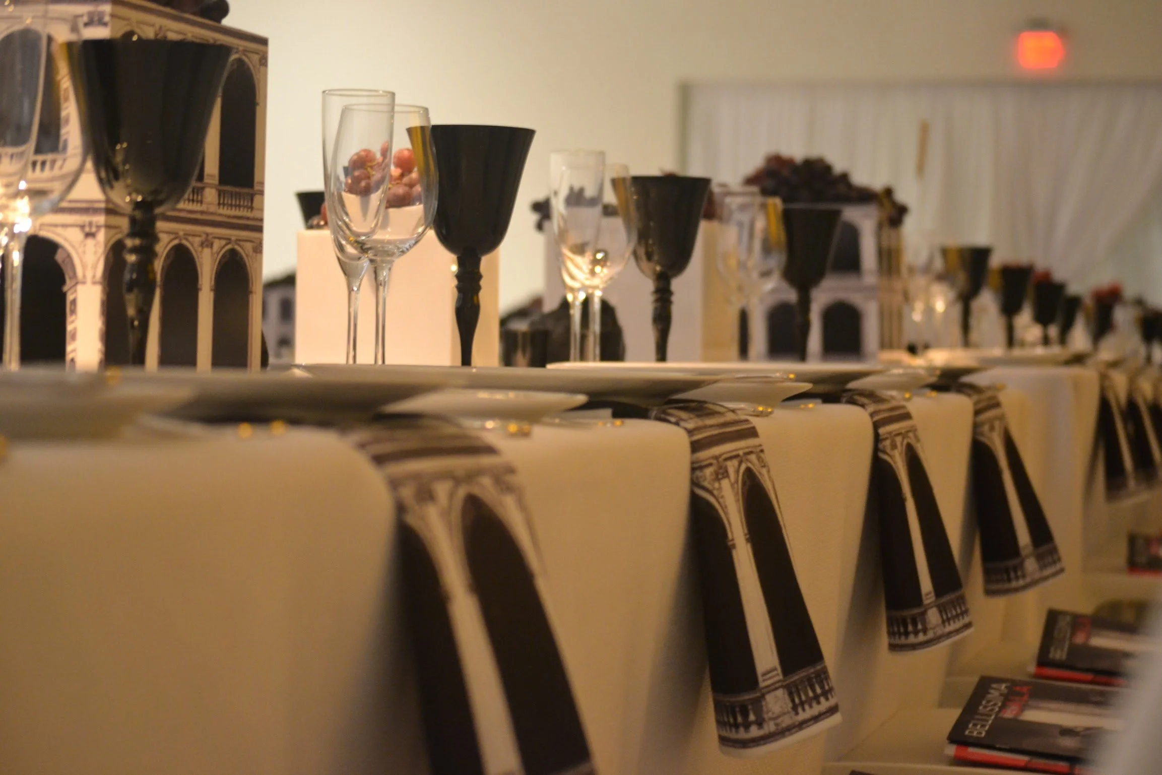 A display of black and clear wine glasses on a table, with restaurant or bar decor in the background.