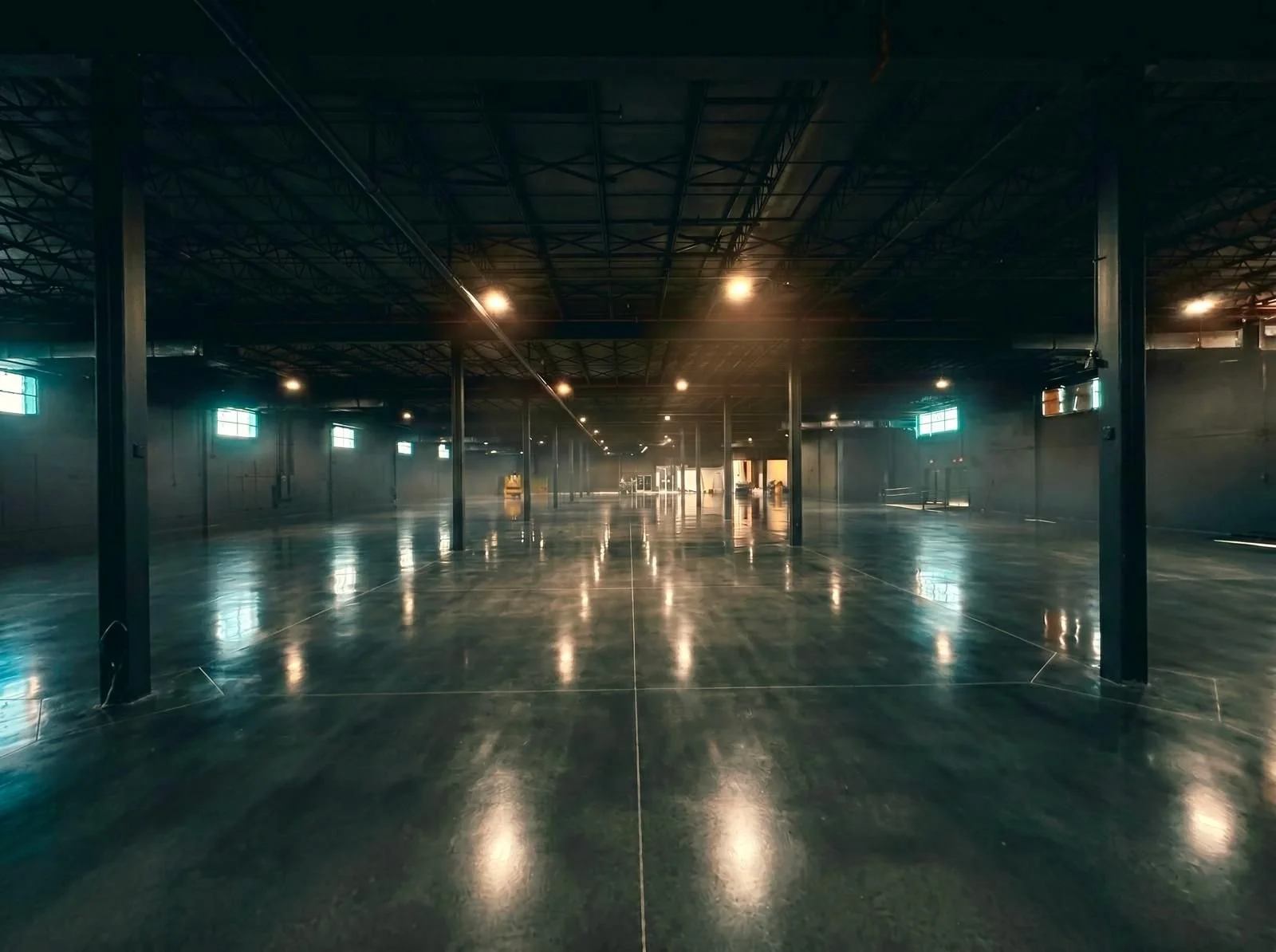 An empty industrial warehouse venue with polished concrete floors, black metal support beams, and small windows letting in natural light.