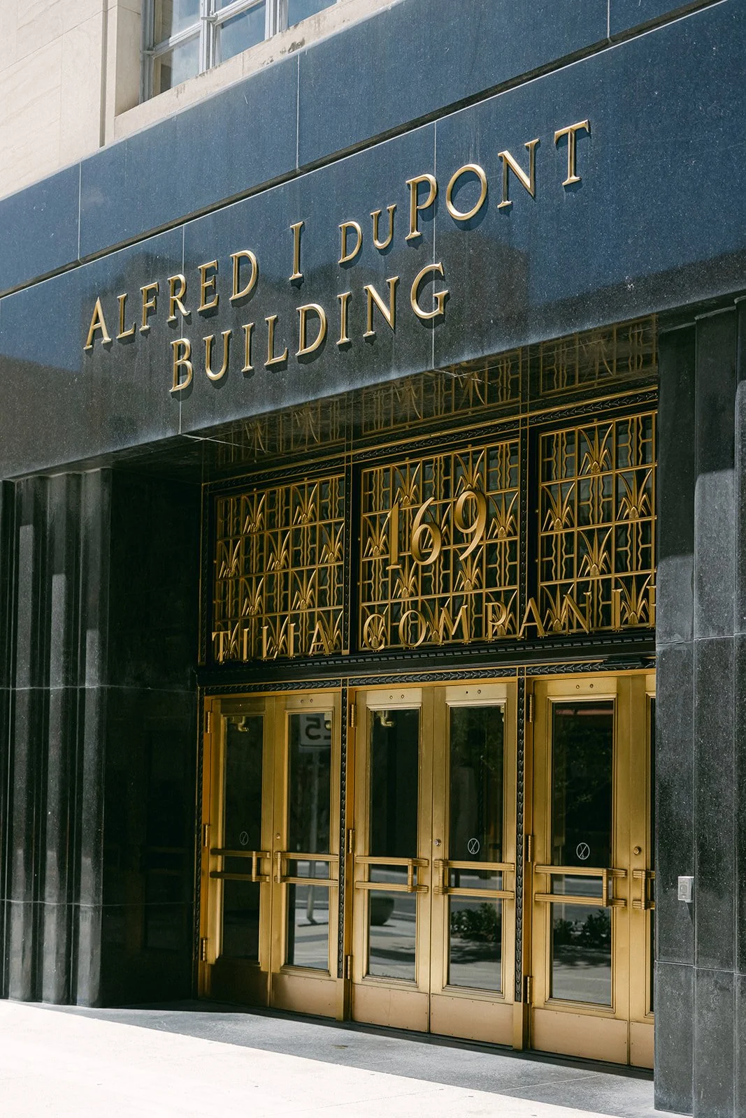 Entrance to the Alfred I. Dupont Building with gold doors and intricate gold gate, and the building's name displayed in gold letters above.