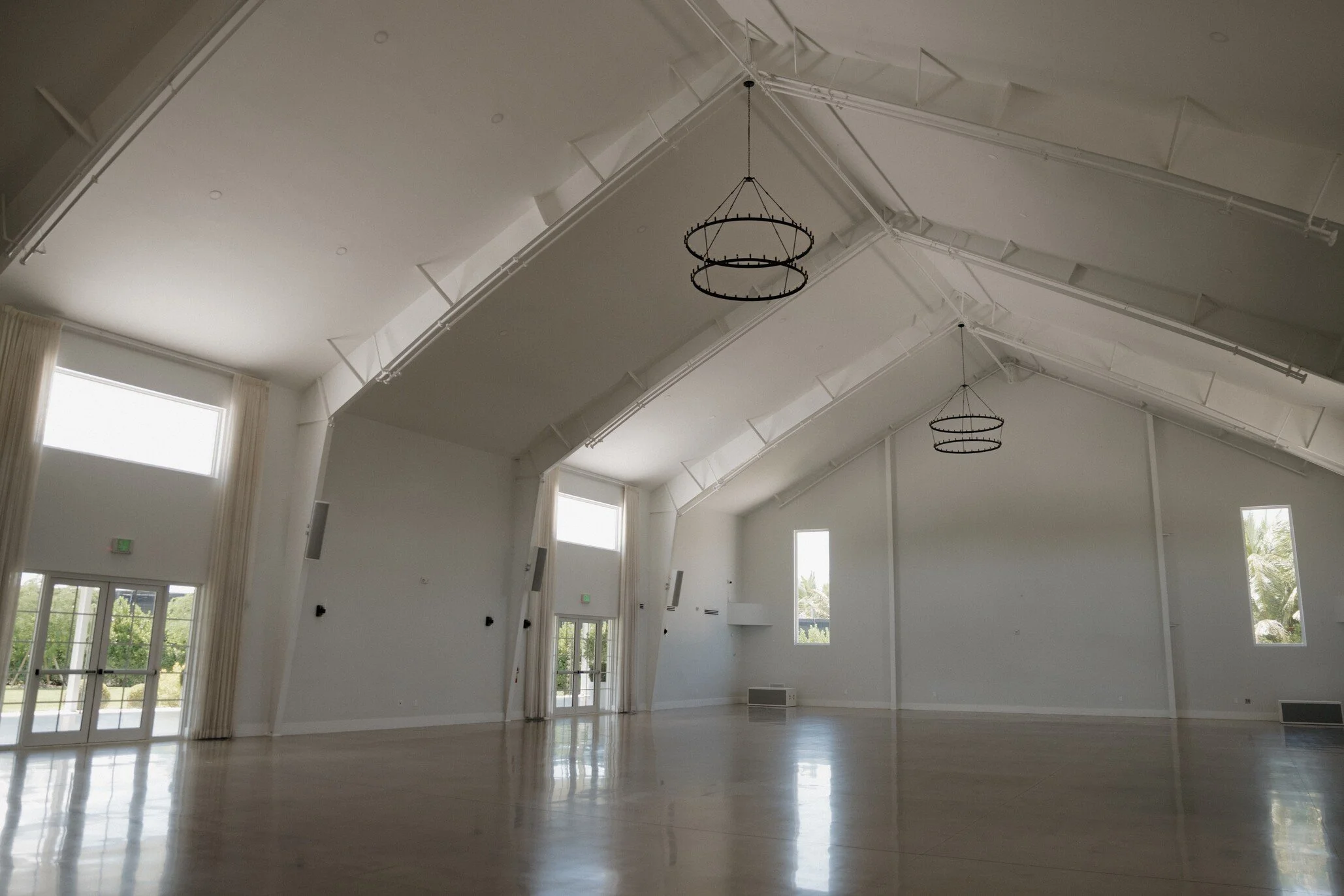 Interior view of a spacious, well-lit room with a high, angled ceiling, large windows, and modern hanging light fixtures.