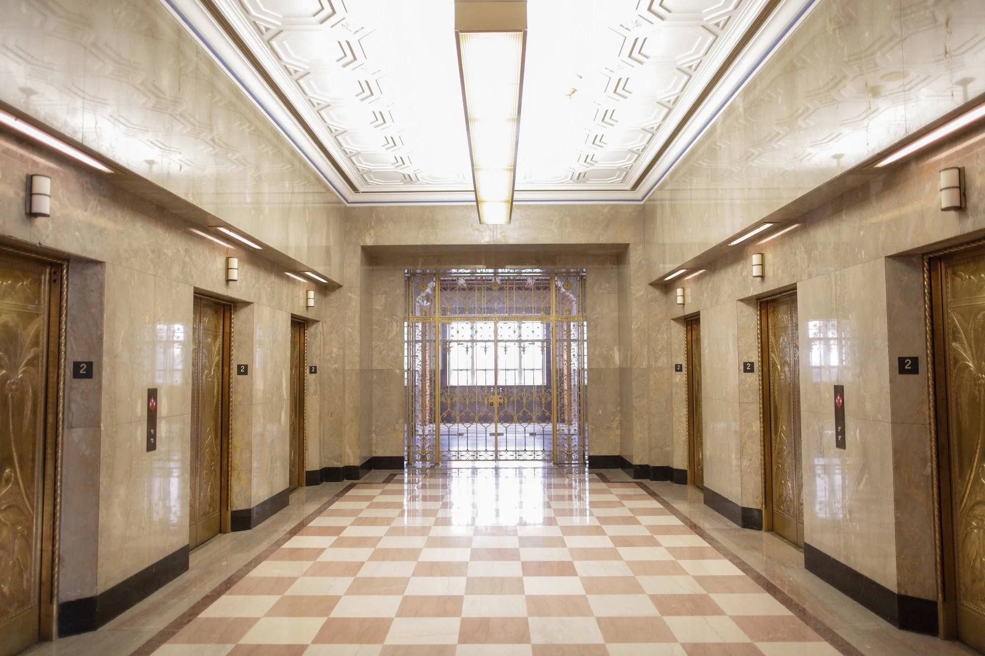Hotel elevator lobby with gold and marble doors, decorative lighting, and a large window at the far end.