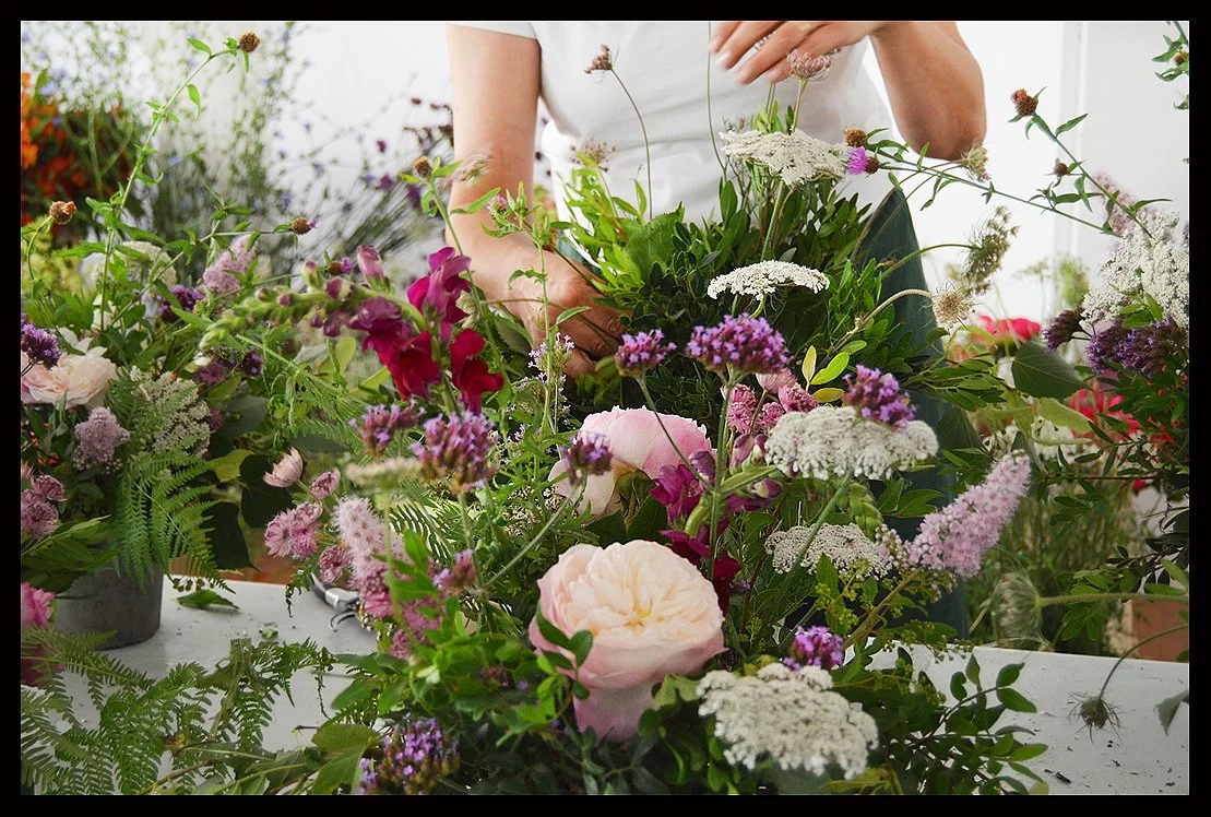 Person arranging a colorful bouquet of pink, white, purple, and green flowers with various greenery.