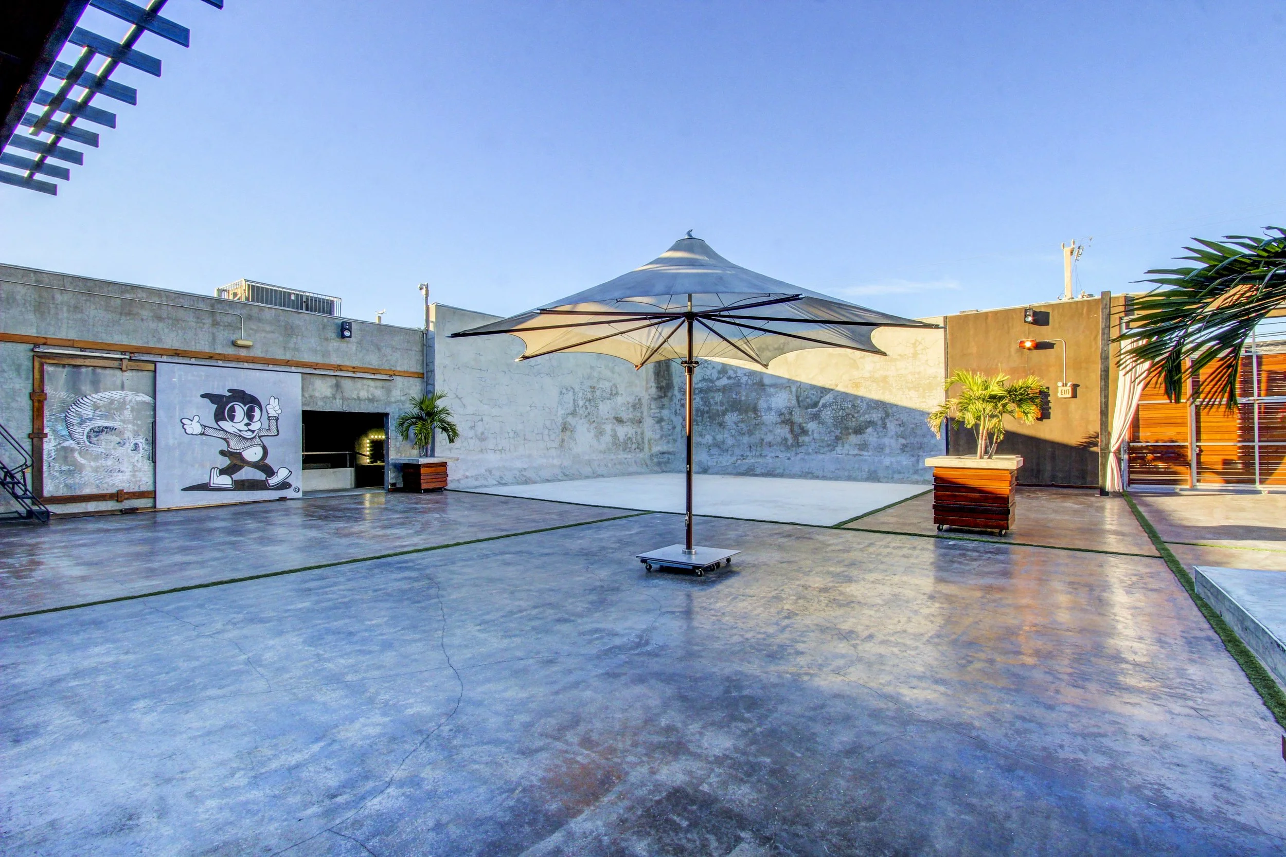 Outdoor patio with a patio umbrella, potted plants, and artwork on the wall, under a clear blue sky.