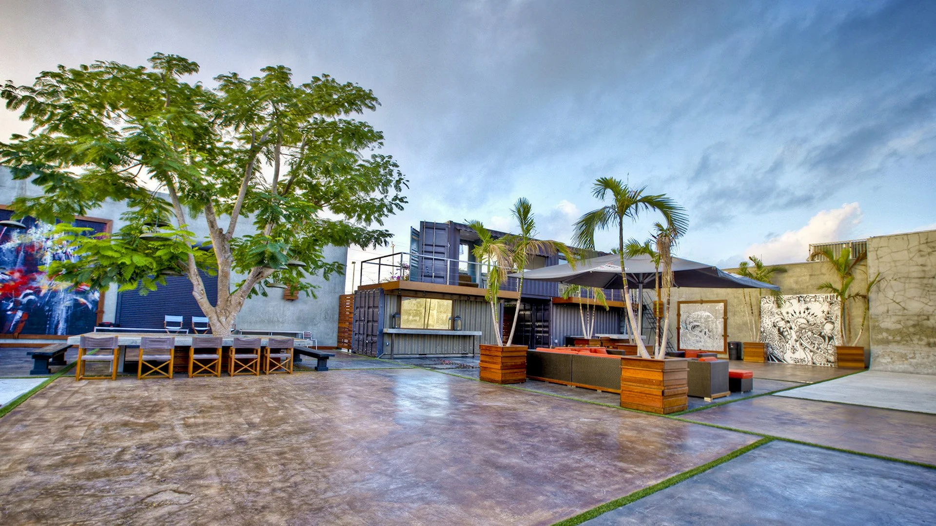 Outdoor venue in Wynwood, Miami with patio area seating, tables, palm trees, and artwork under a cloudy sky.
