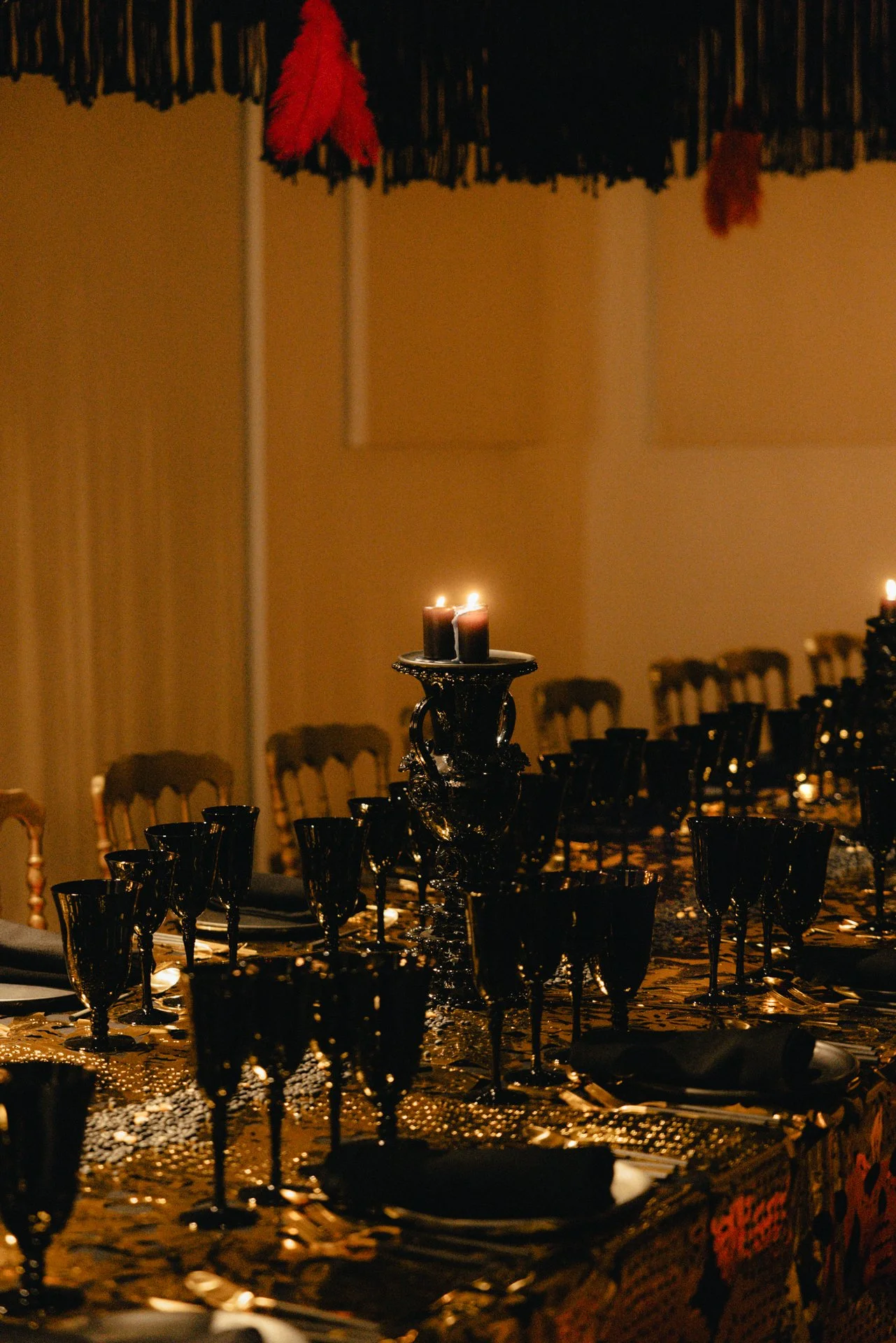 A dining table setup with black glassware and a tall decorative candle holder with lit candles, in a dimly lit room with a dark, elegant ambiance.