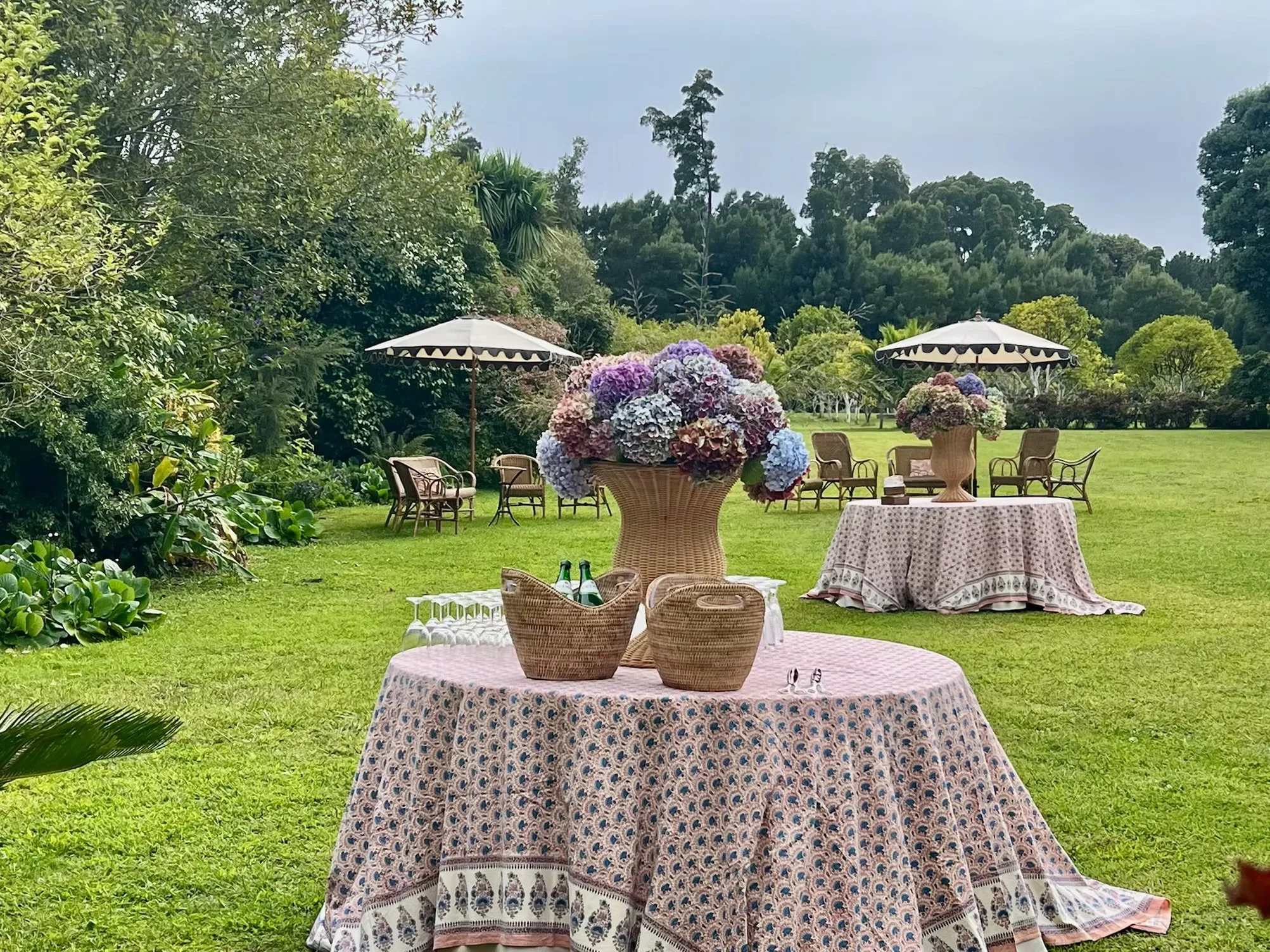Outdoor garden setting  at the Convento de Cabanas with tables, chairs, umbrellas, and large floral arrangements on tables, surrounded by lush greenery and trees.