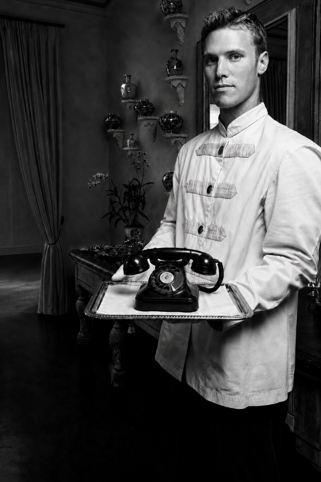 waiter holding old fashioned telephone on silver tray in white linen apparel