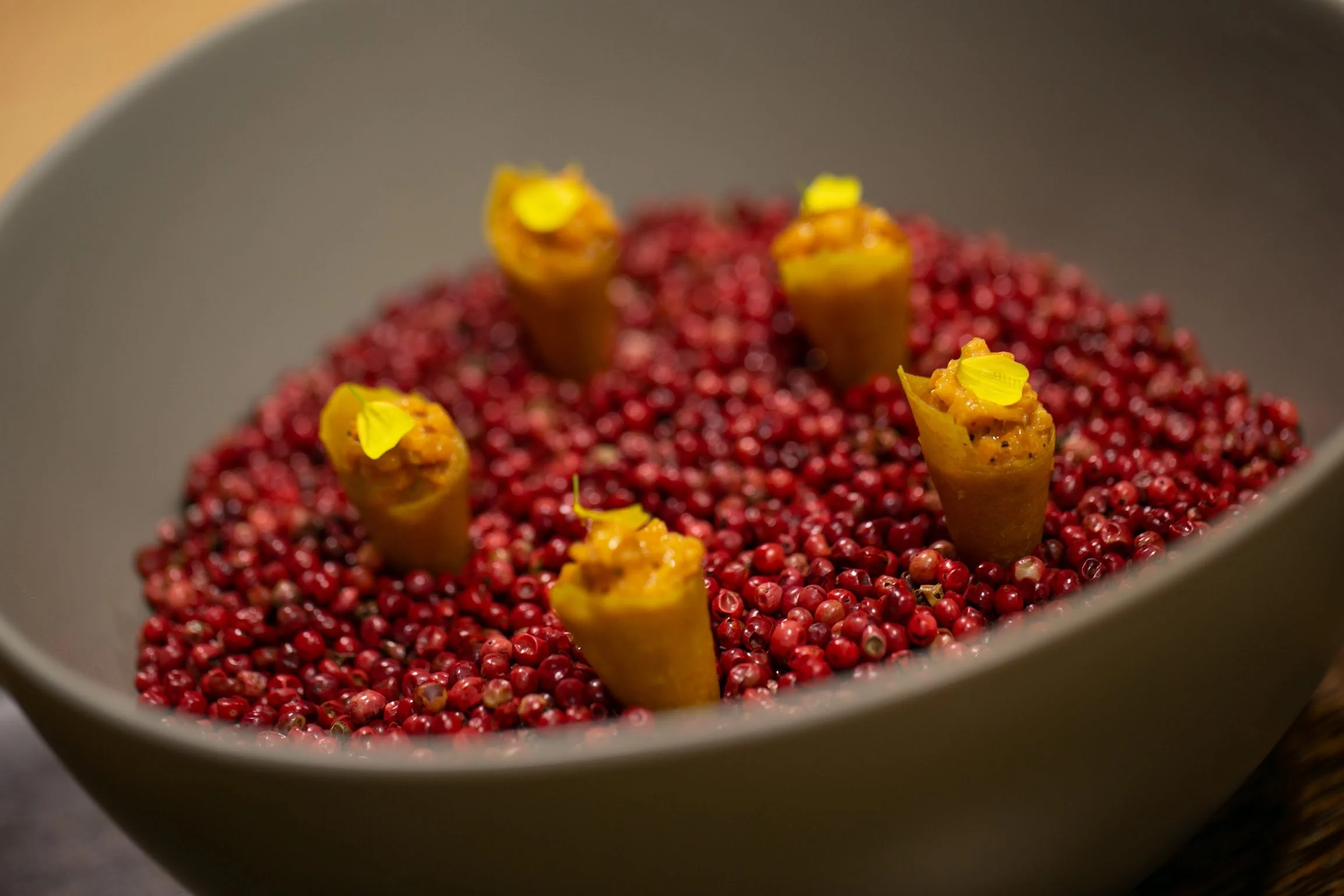 Chef's taste of the seasons caviar dishes, featuring bright red caviar, topped with yellow flower petals in a gray bowl.