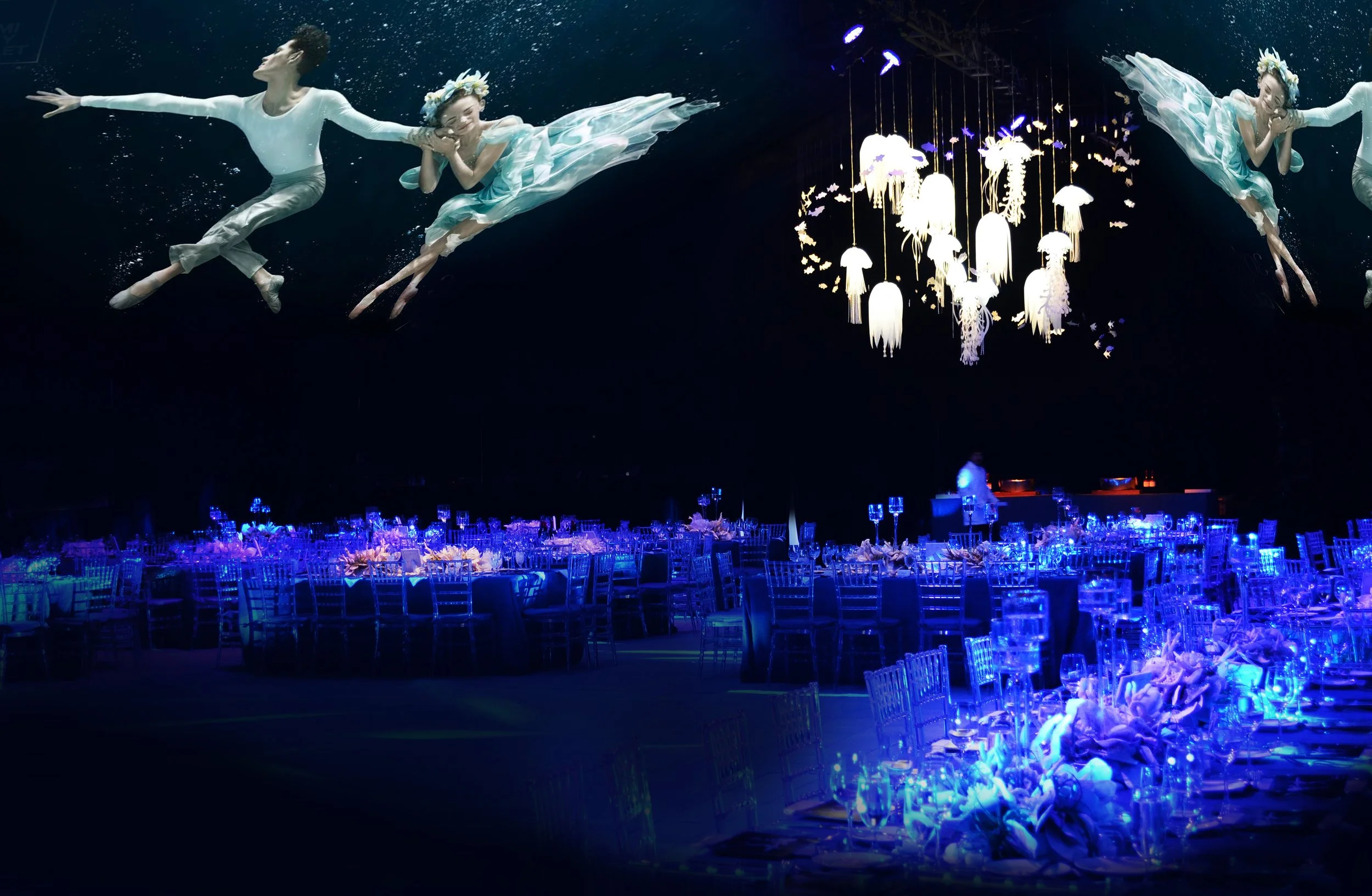 Underwater scene with two dancers in flowing costumes and floral headpieces, floating amidst glowing jellyfish and illuminated seating arrangements.