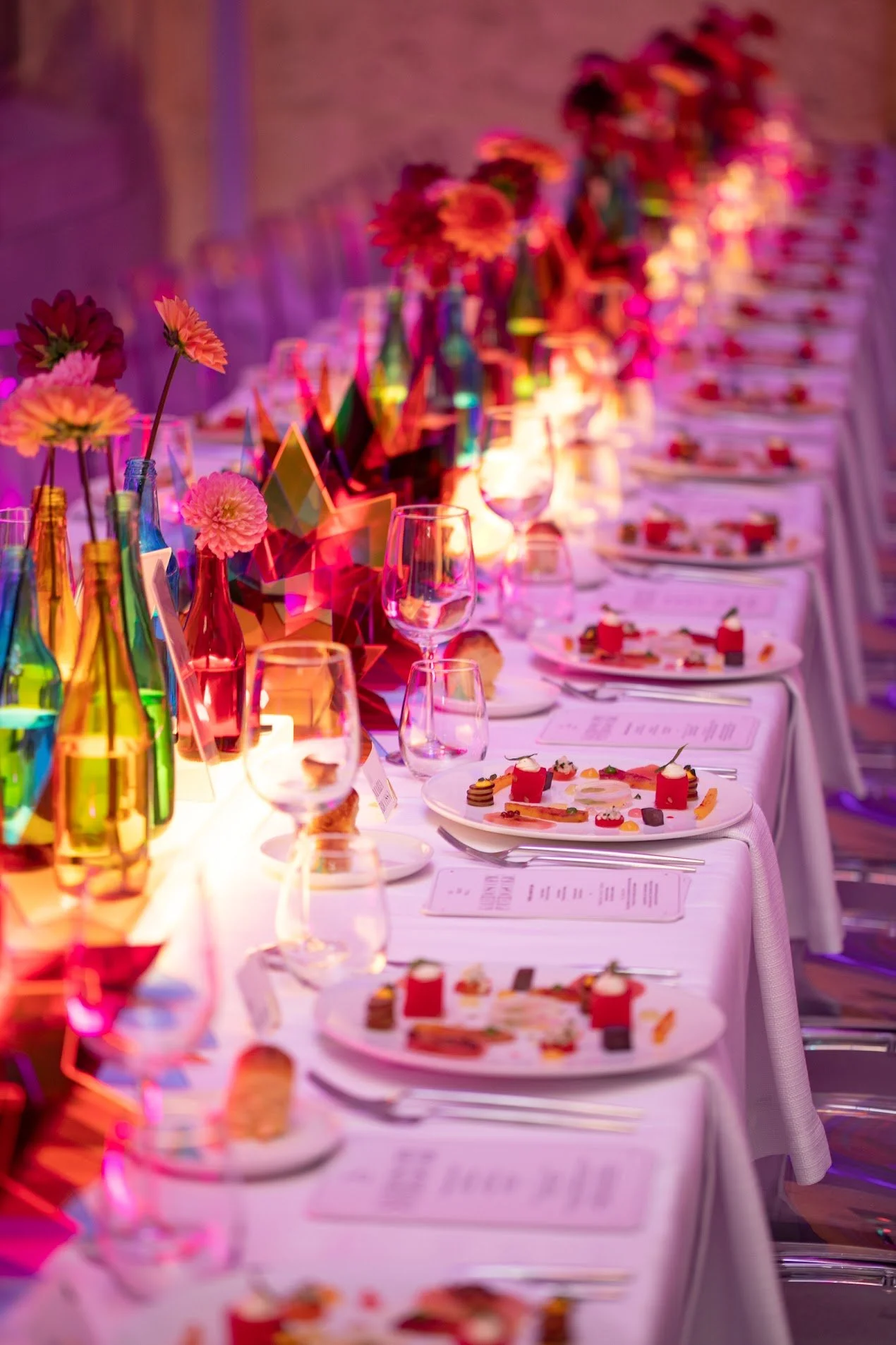 A long dining table decorated with colorful vases, flowers, and star-shaped centerpieces, set with plates, glasses, and utensils for a formal event.