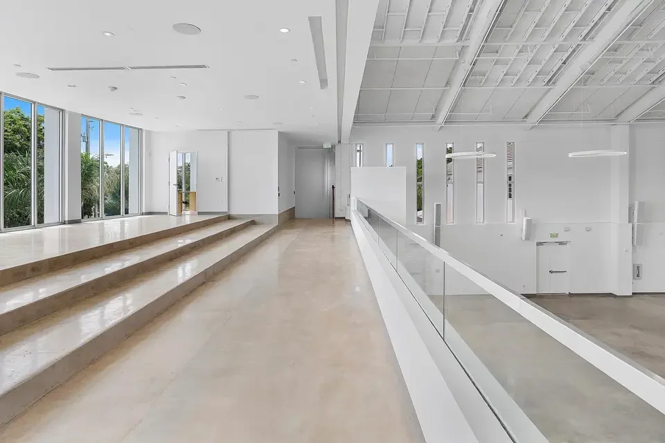 Modern interior space with large windows, white walls, wooden floors, and tiered seating.